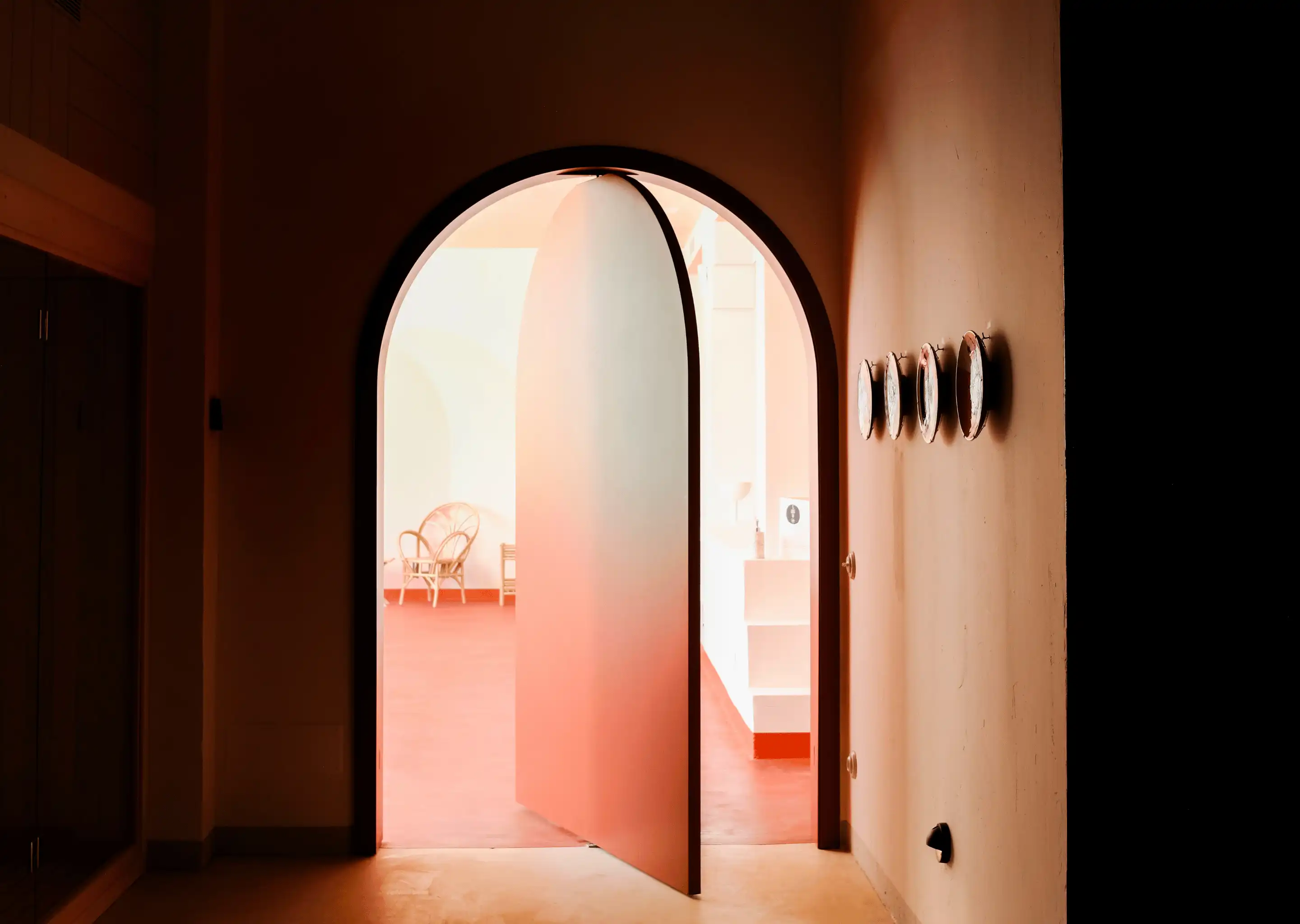 Curved door opening into a bright room with a wicker chair and terracotta floor.