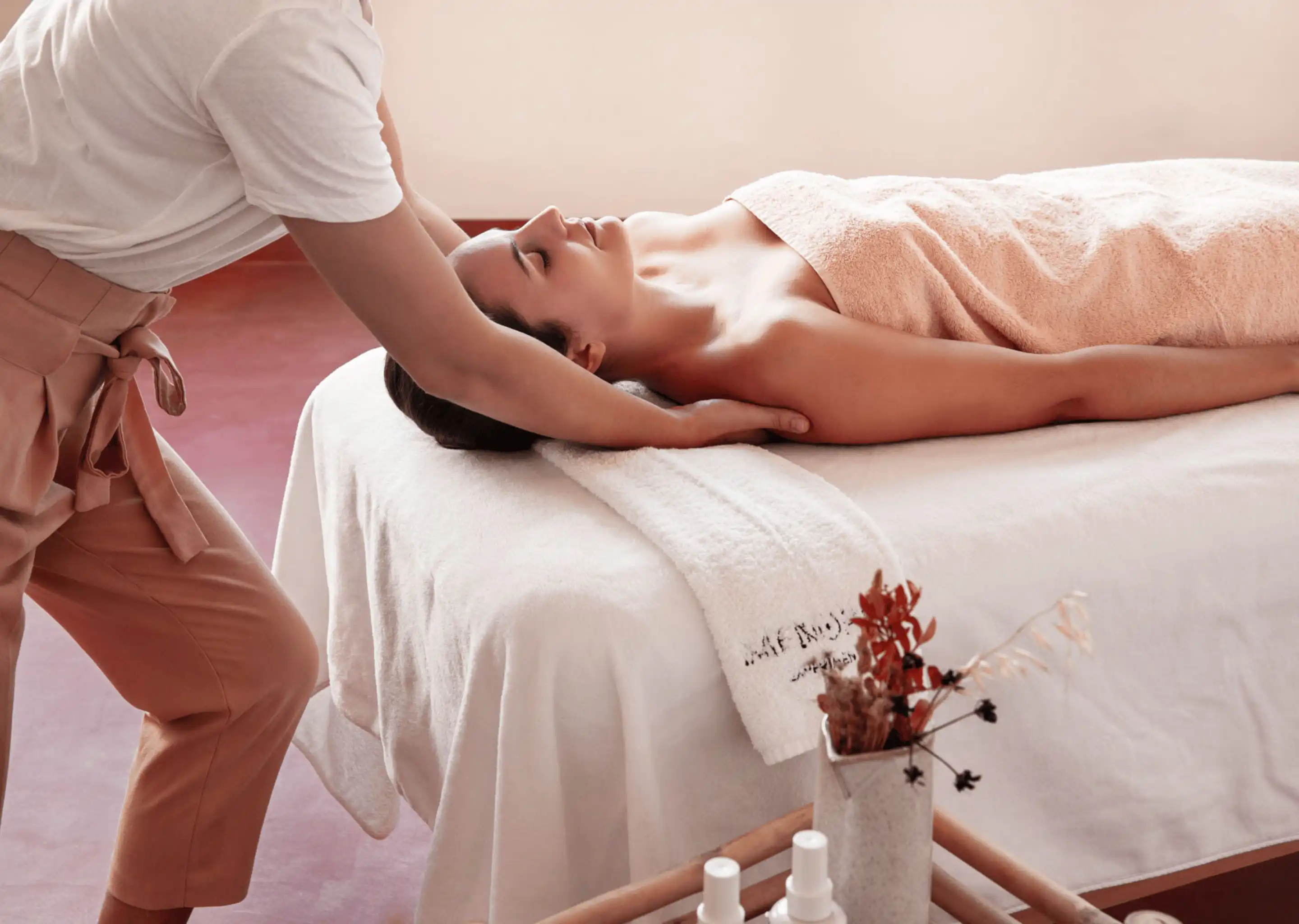 Woman receiving a relaxing neck and shoulder massage on a spa bed covered with white towels.