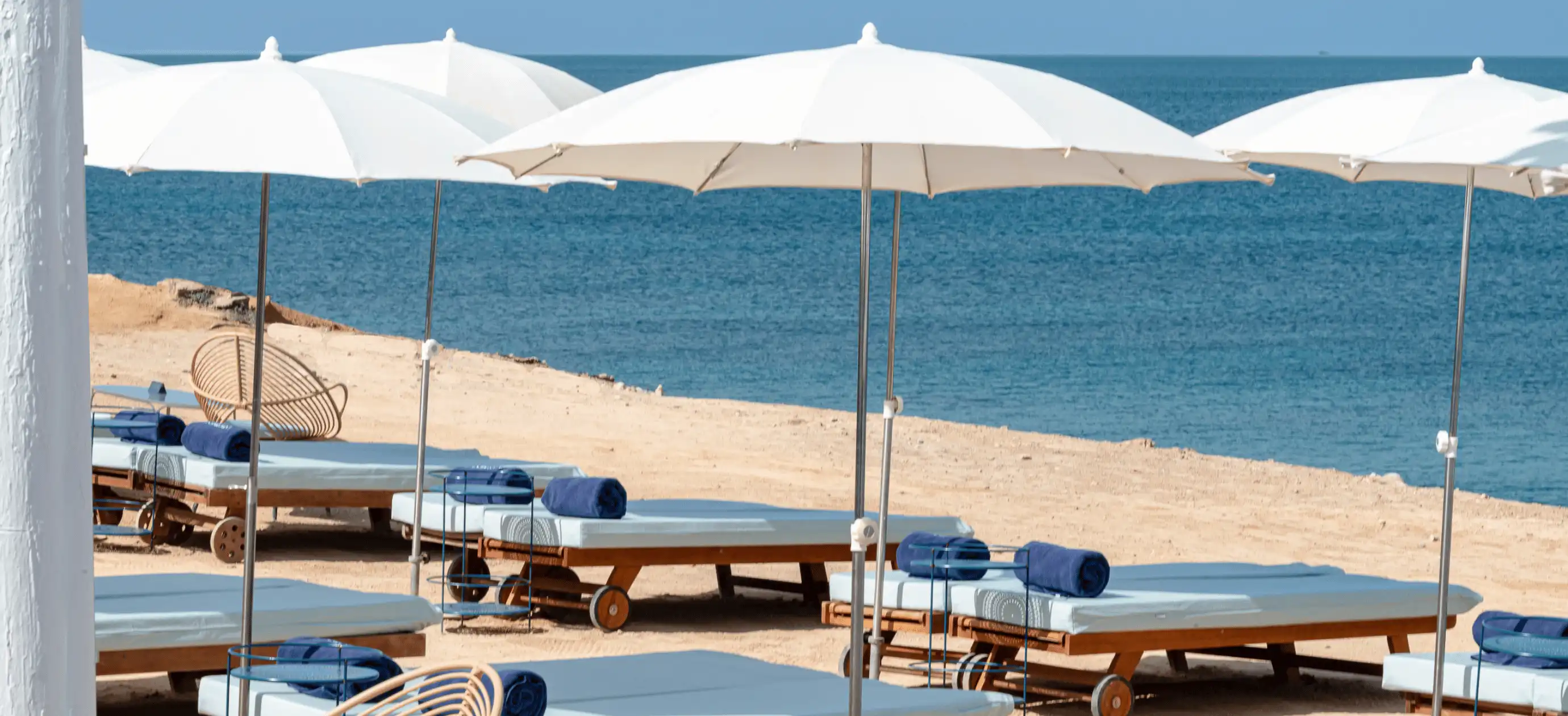 Beach loungers with blue towels under white umbrellas on sandy shore by calm blue sea.