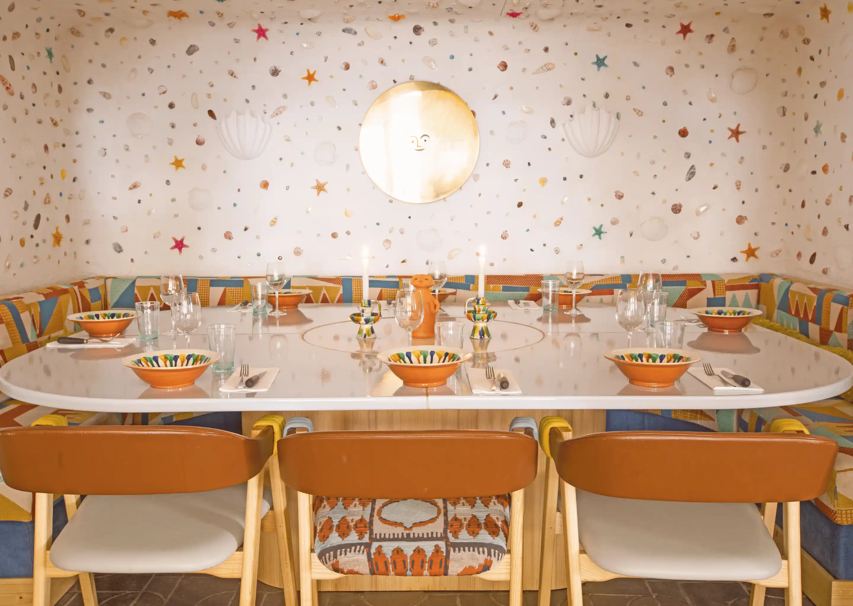Dining table set with colorful bowls, glasses, and candles in a cozy room with seashell and starfish wall decorations.