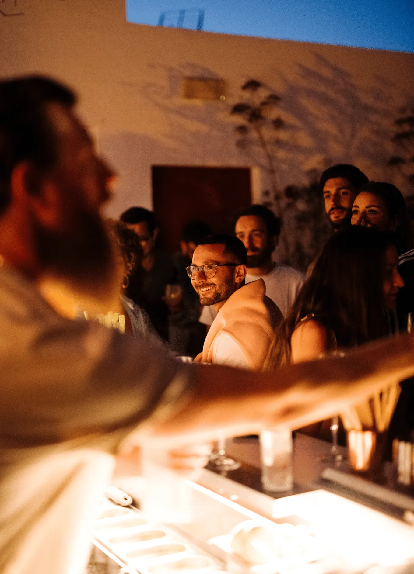 Group of young adults socializing warmly at an outdoor bar during twilight.
