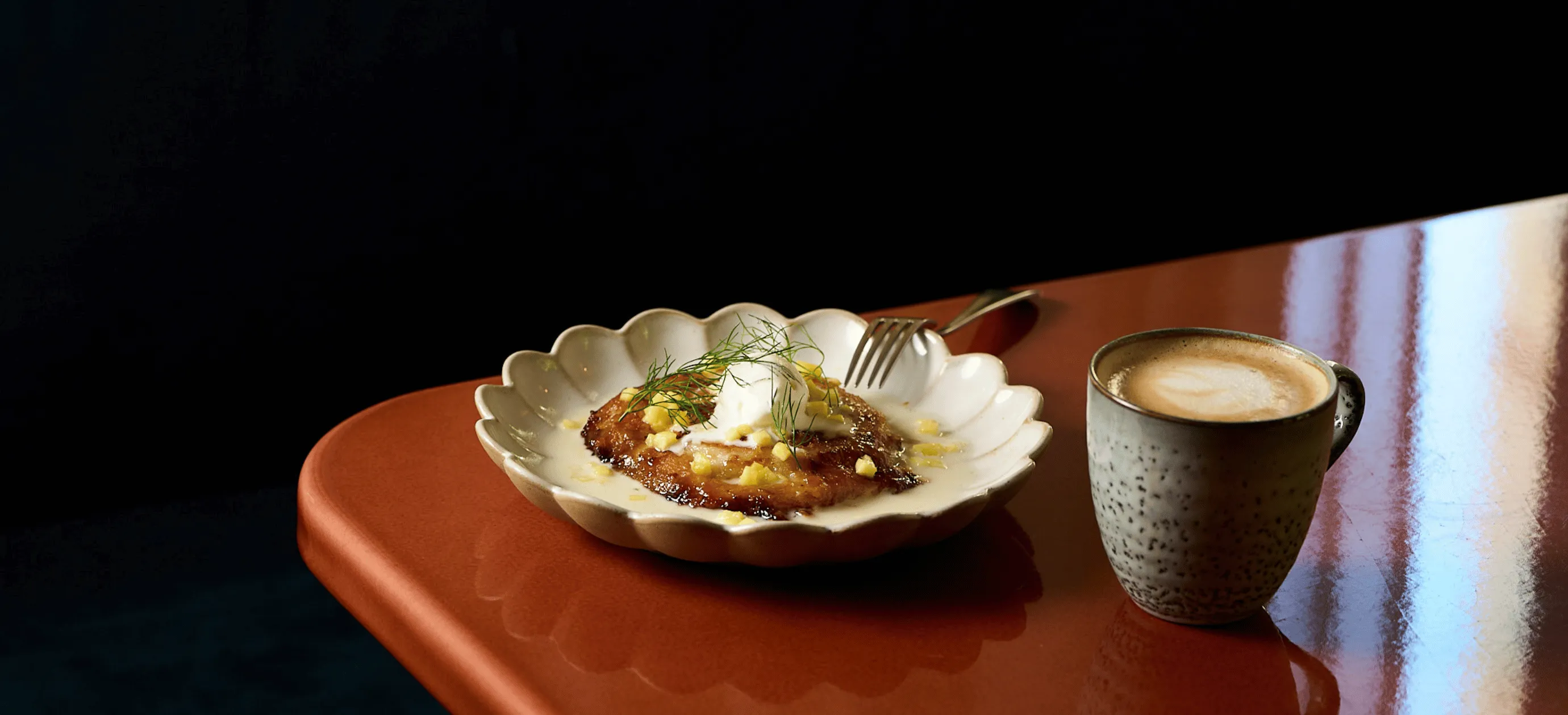 Plate with a cream-topped dessert garnished with herbs and a cup of coffee on a glossy brown table.
