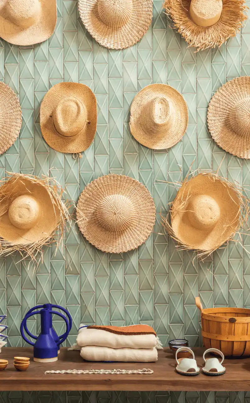 Wall display of woven straw hats above a wooden shelf holding folded textiles, sandals, small bowls, and a wooden bucket.