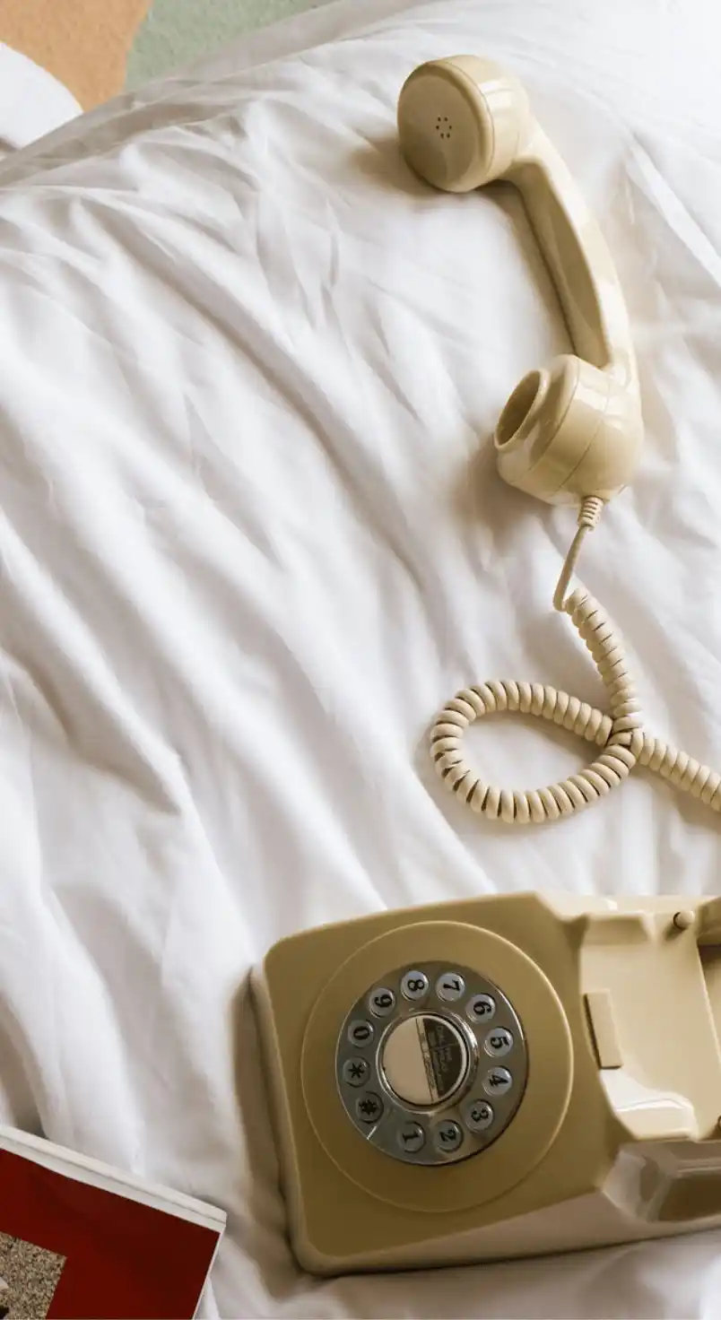 Beige rotary dial telephone handset resting on white bedsheets.