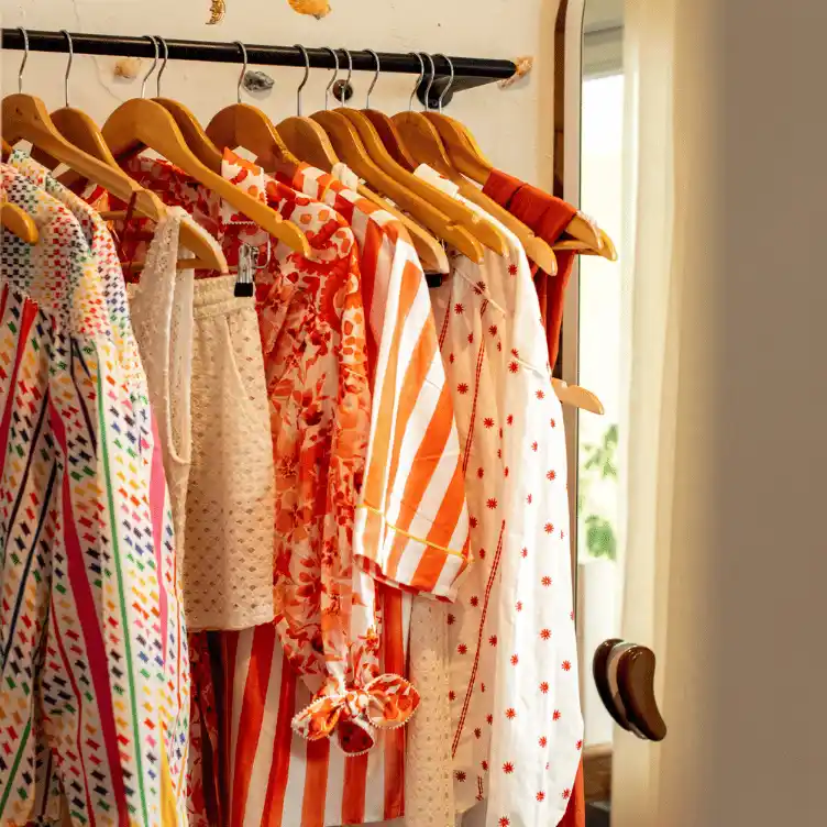 Wooden hangers displaying colorful patterned and striped clothes on a black metal rack near a mirror and a door handle.