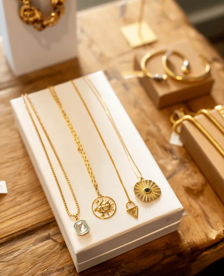 Four gold necklaces with different pendants displayed on a white box on a wooden surface.