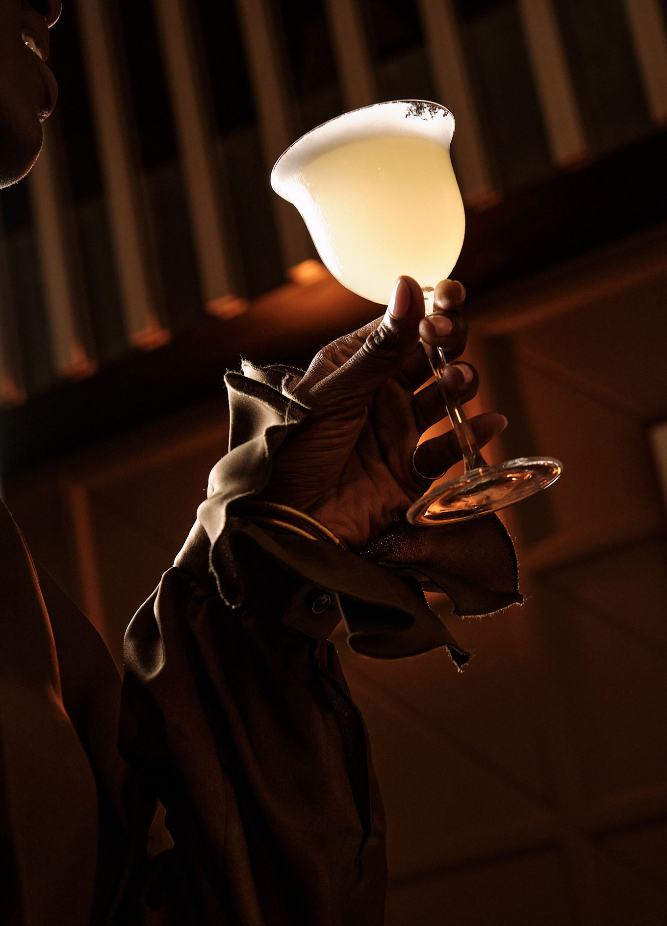 Hand holding a cocktail glass with a light yellow drink and a salted rim in a dimly lit setting.