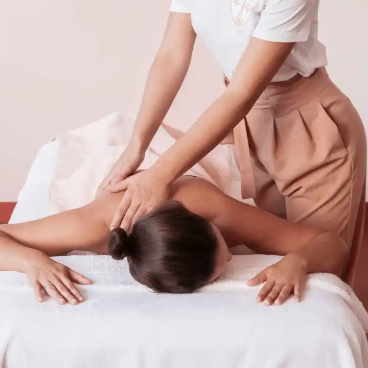 Person receiving a back massage while lying face down on a white massage table.