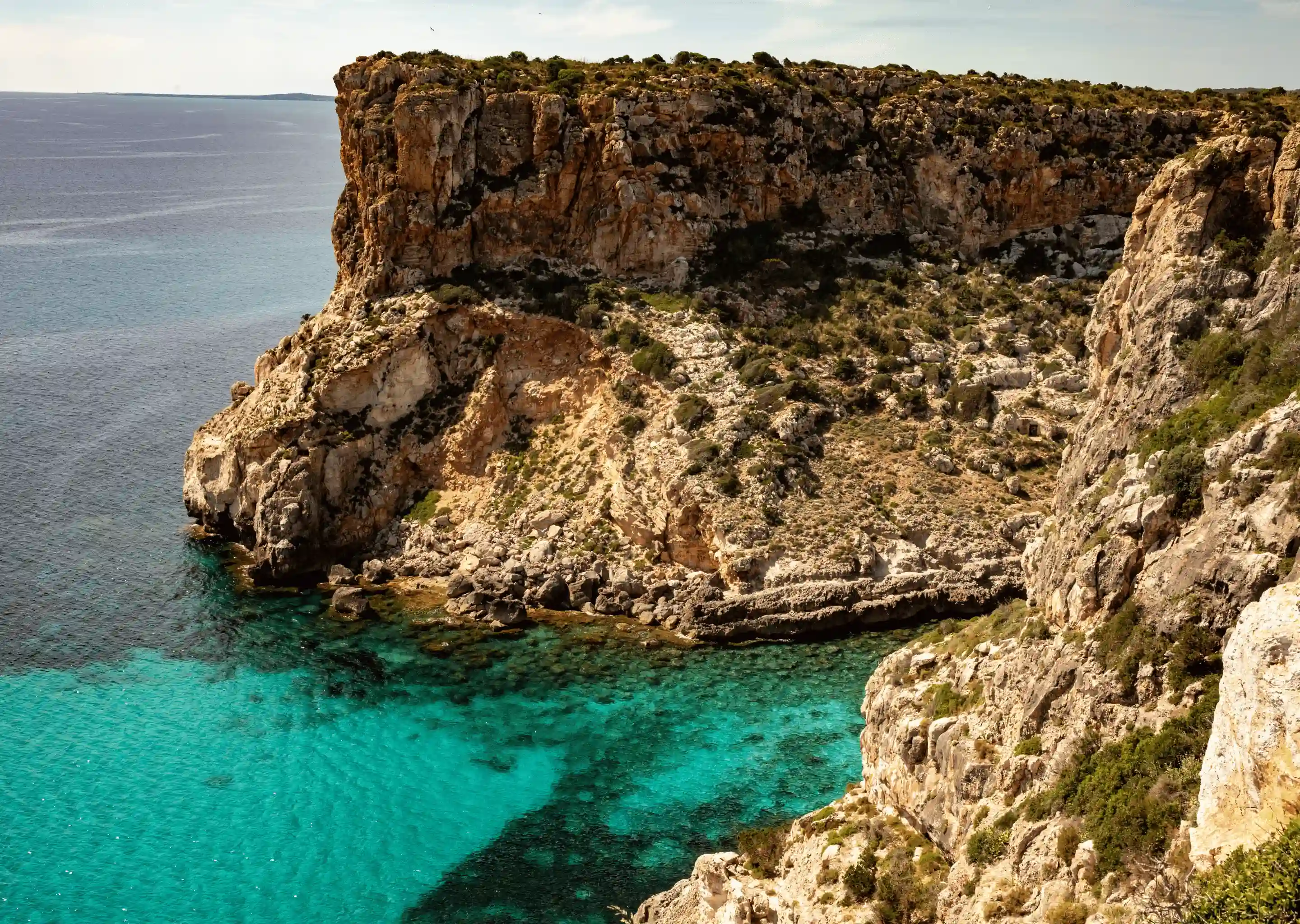 Rocky coastal cliffs overlooking clear turquoise sea water.