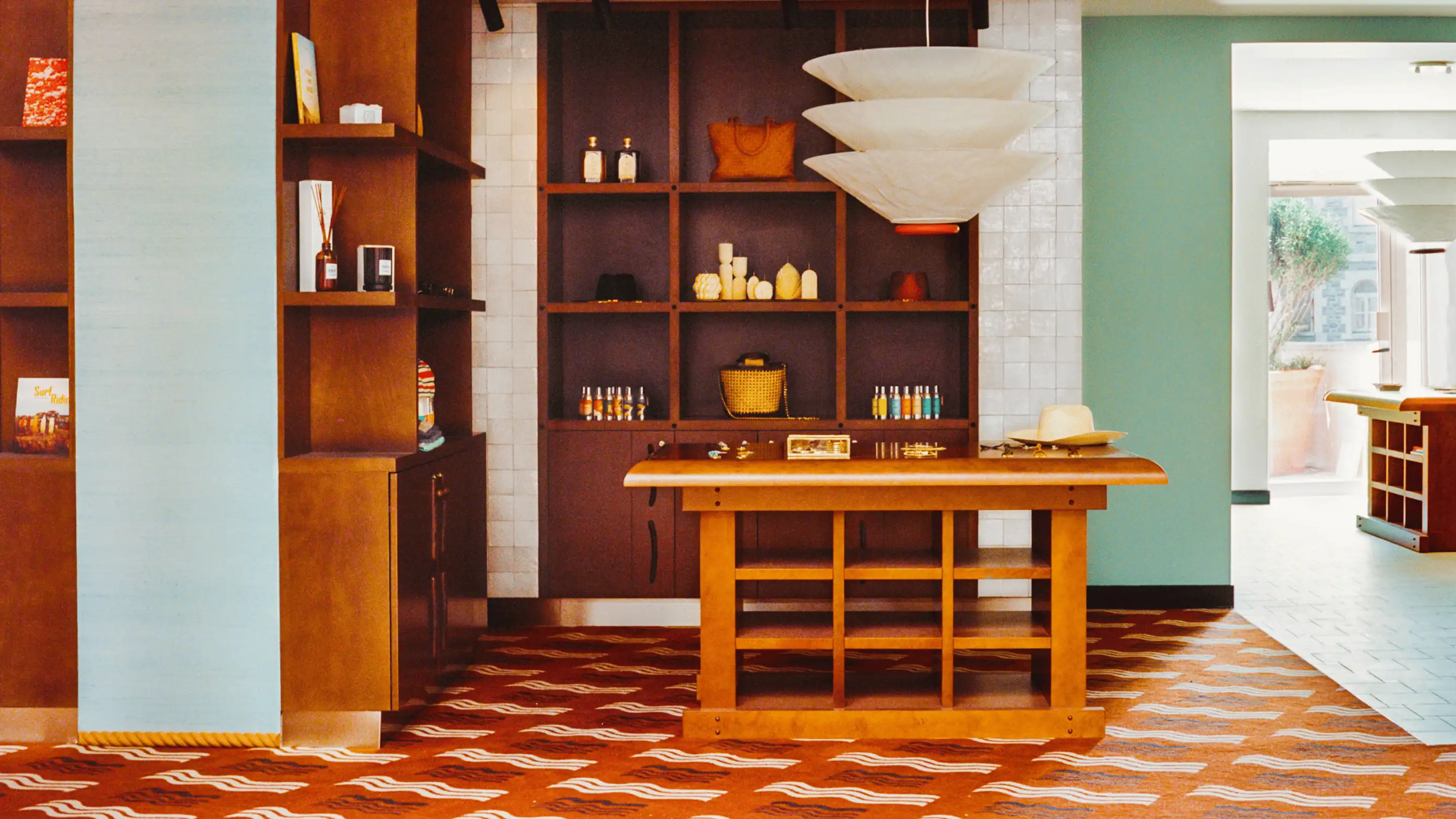 Boutique hotel gift shop with wooden shelves and table displaying various items including candles, bottles, and a hat.