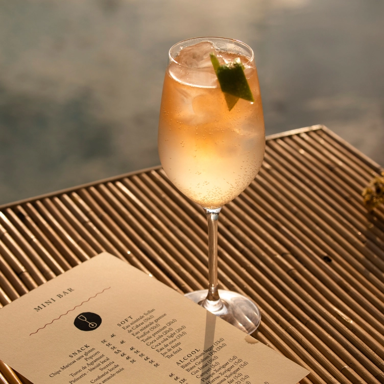 Glass of iced cocktail garnished with a lime wedge on a table next to a mini bar menu.