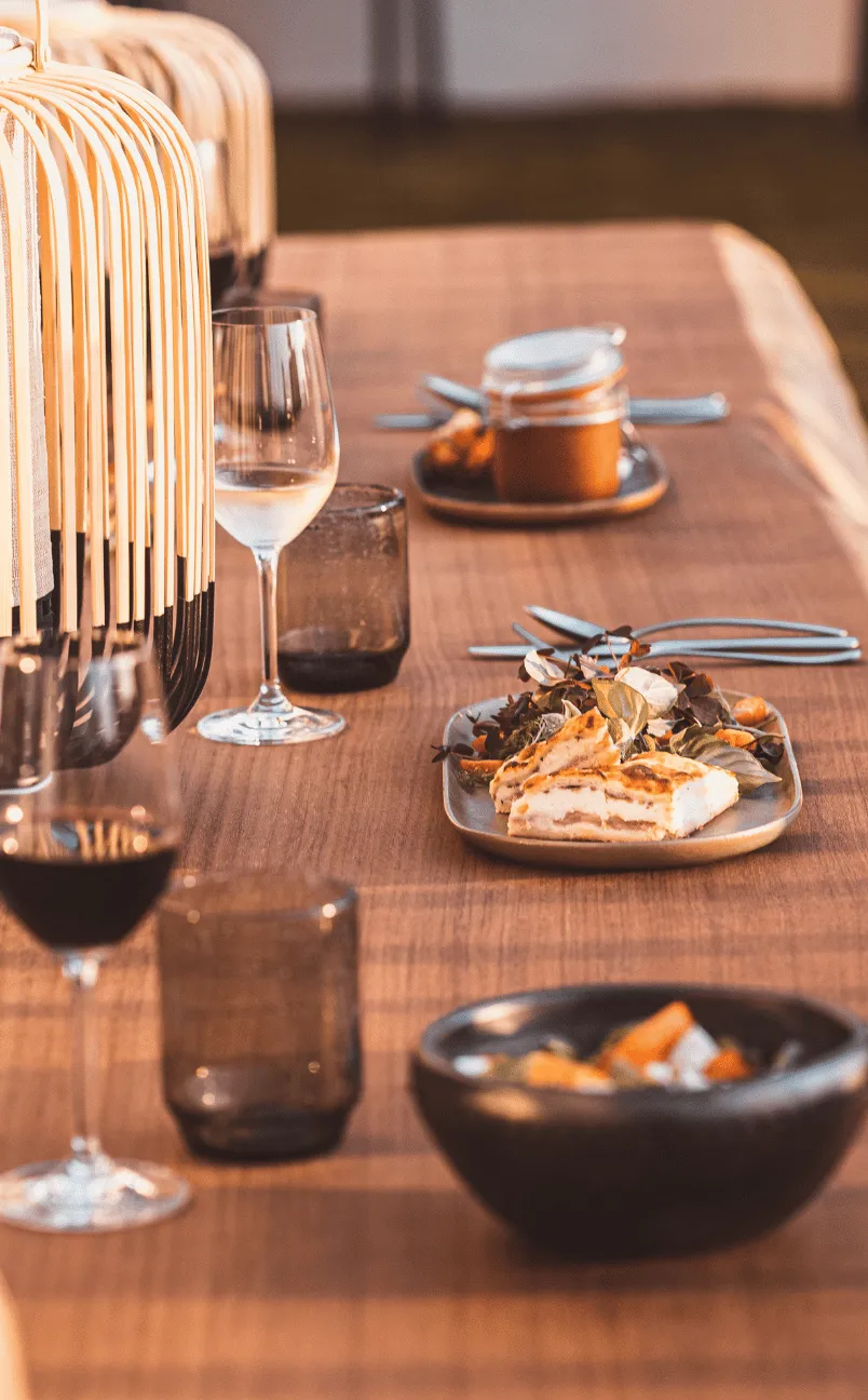 Set da tavola in legno con piatti di cibo, bicchieri da vino e lanterne decorative.