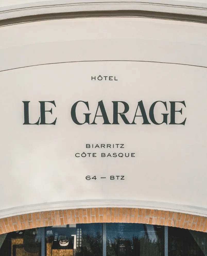 Hotel Le Garage sign on a white curved wall with brick arch above windows.