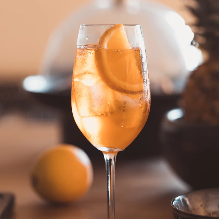Glass of iced orange cocktail with an orange slice garnish on a table.