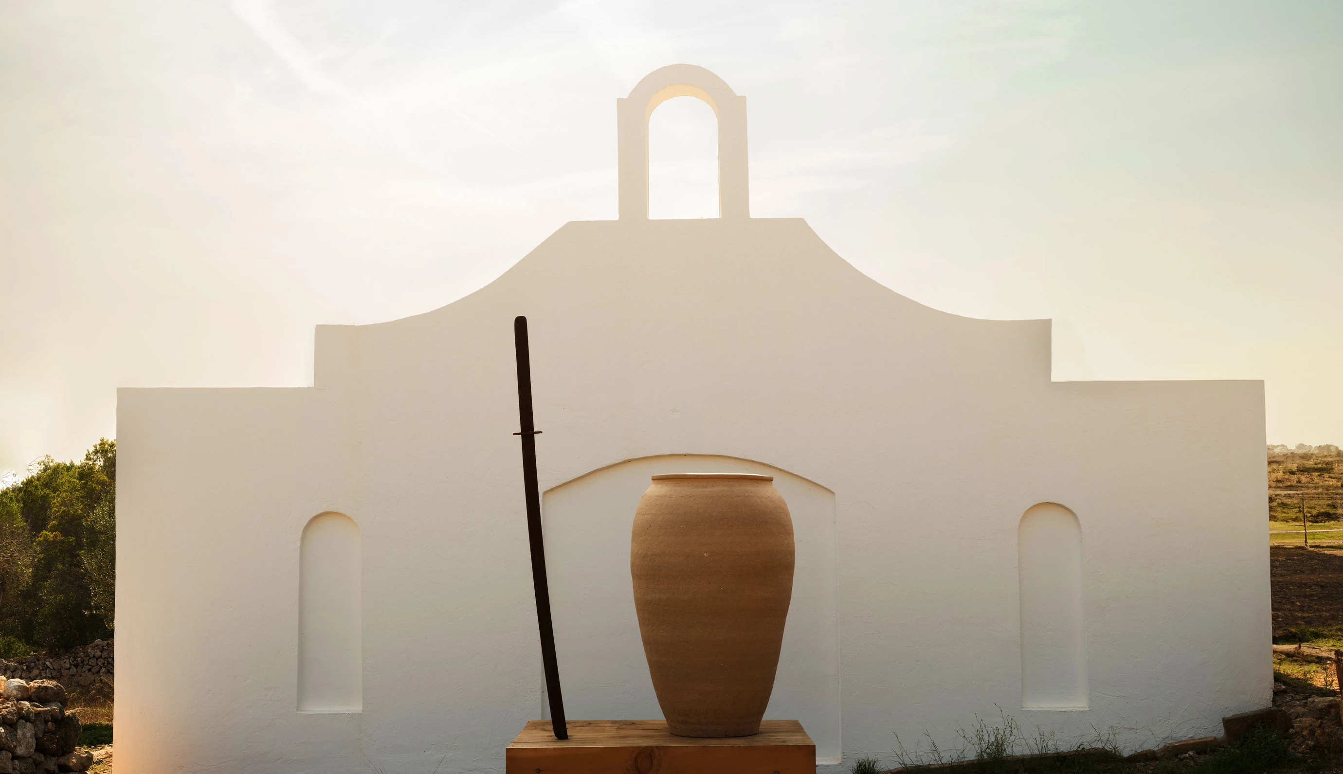 Arredamento minimalista con un barattolo di terracotta e un oggetto scultoreo davanti a una parete bianca immacolata di Experimental Group.
