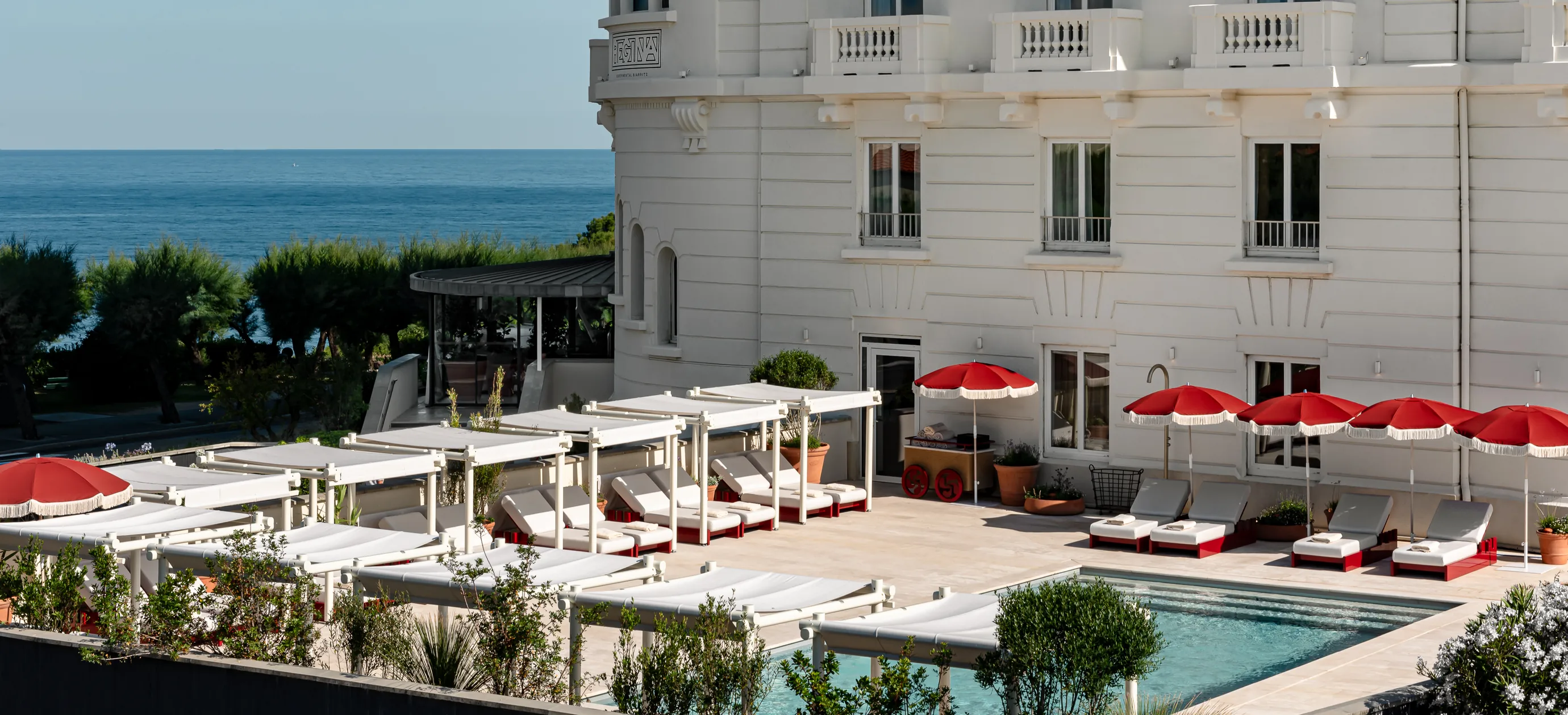 Piscina all'aperto con lettini e ombrelloni rossi di fronte all'hotel Experimental Group a Biarritz, sulla costa basca.