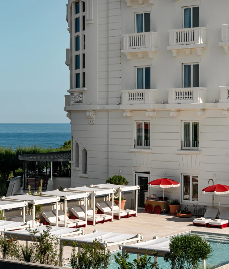 Vista esterna dell'architettura storica e della terrazza a bordo piscina dell'Hôtel Régina Experimental, con vista sull'oceano a Biarritz.