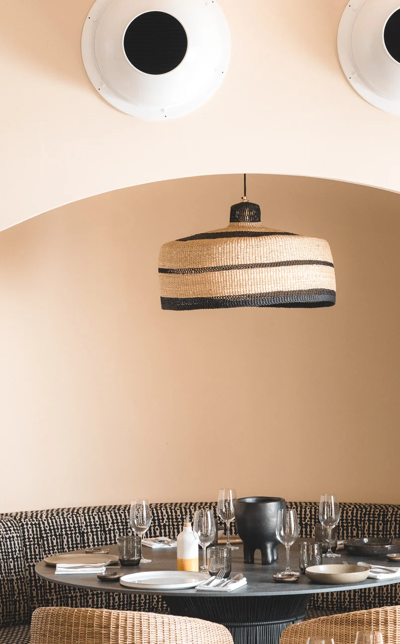 Elegant round dining table setup in a curved alcove with a woven pendant lamp at Hôtel Le Garage, Biarritz.