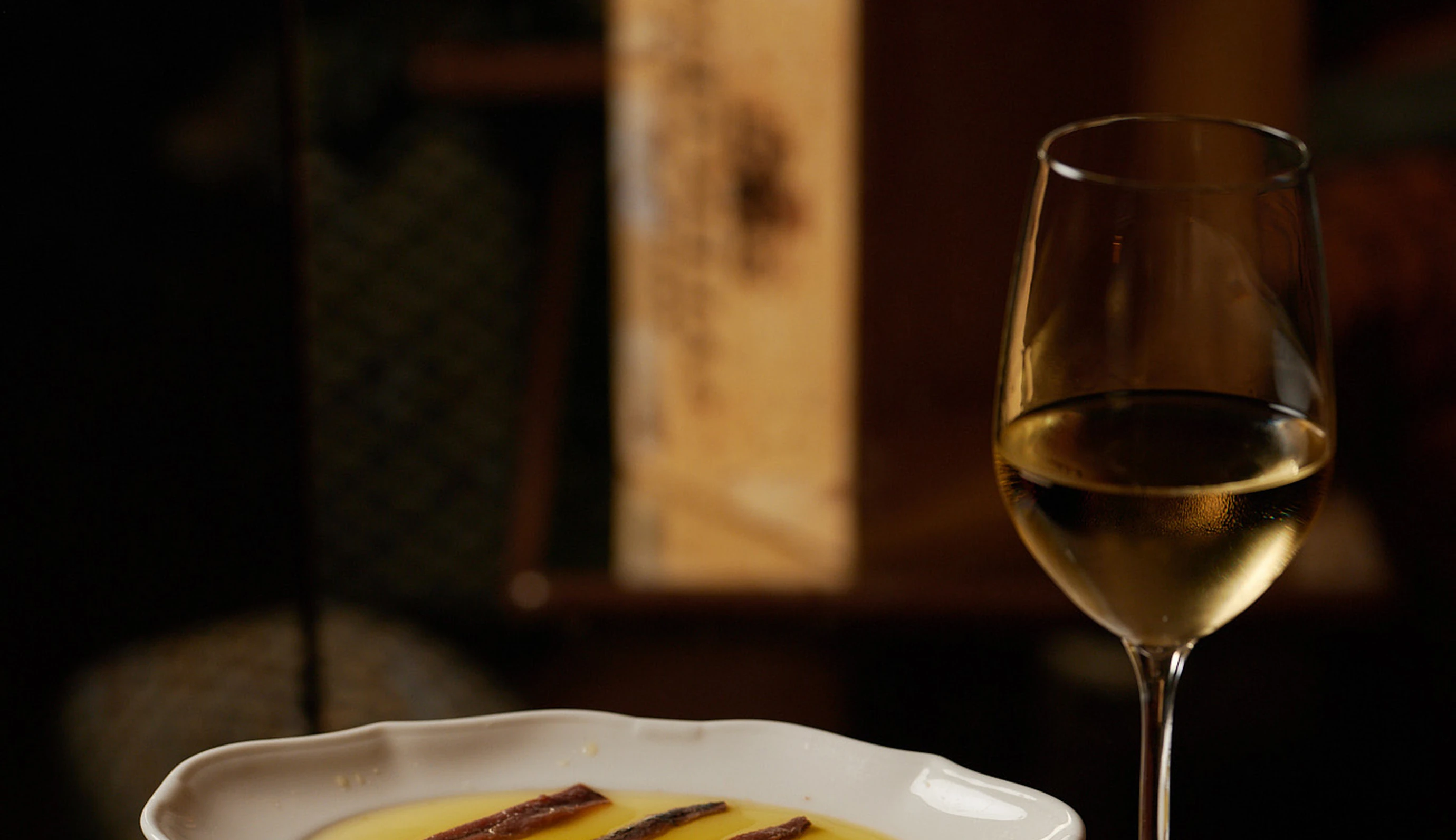 Close-up of a glass of white wine and a plate of anchovies, gastronomic experience at La Compagnie bar, Experimental Group.
