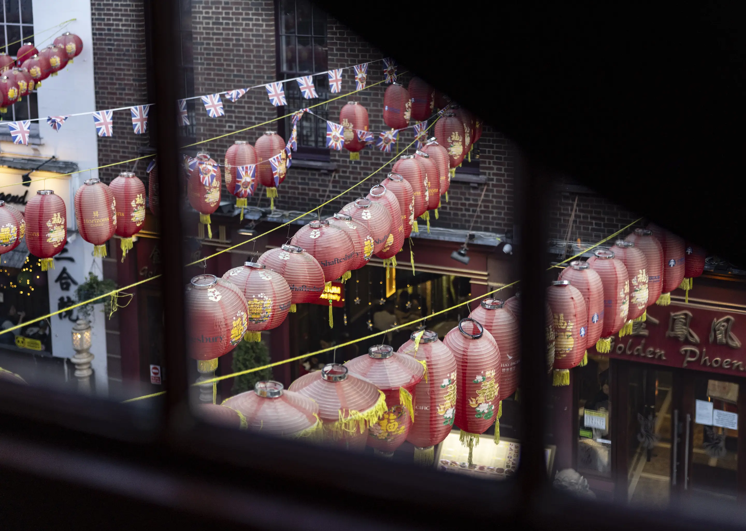 Traditional red lanterns hanging over a lively street seen from indoors, Chinatown, London.