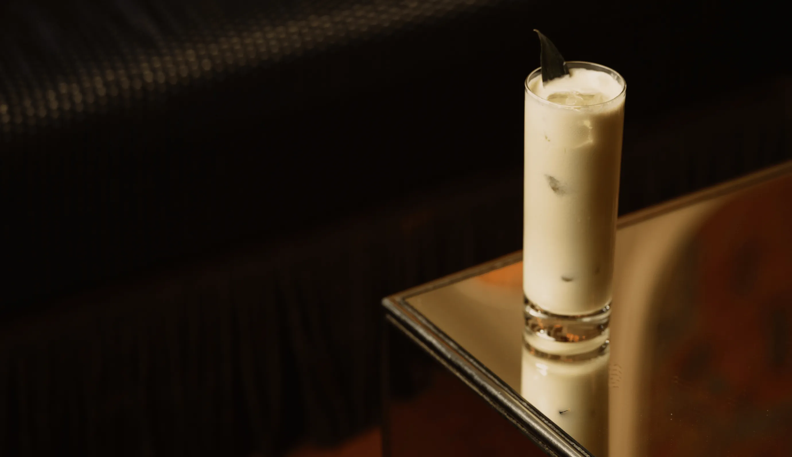 Creamy craft cocktail in a highball glass with a garnish on a mirrored table at Experimental Group.