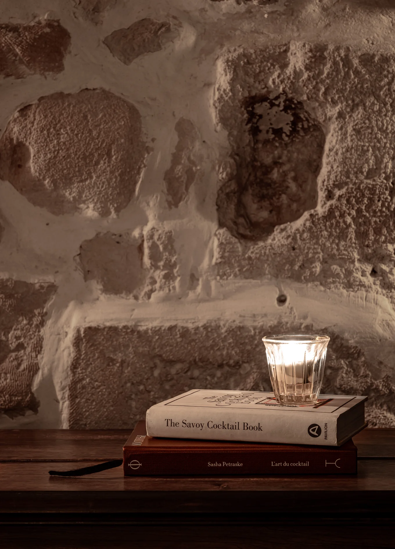 Cozy nook with a candle next to "The Savoy Cocktail Book" and "L'art du cocktail" by Sasha Petraske at an Experimental Group establishment.