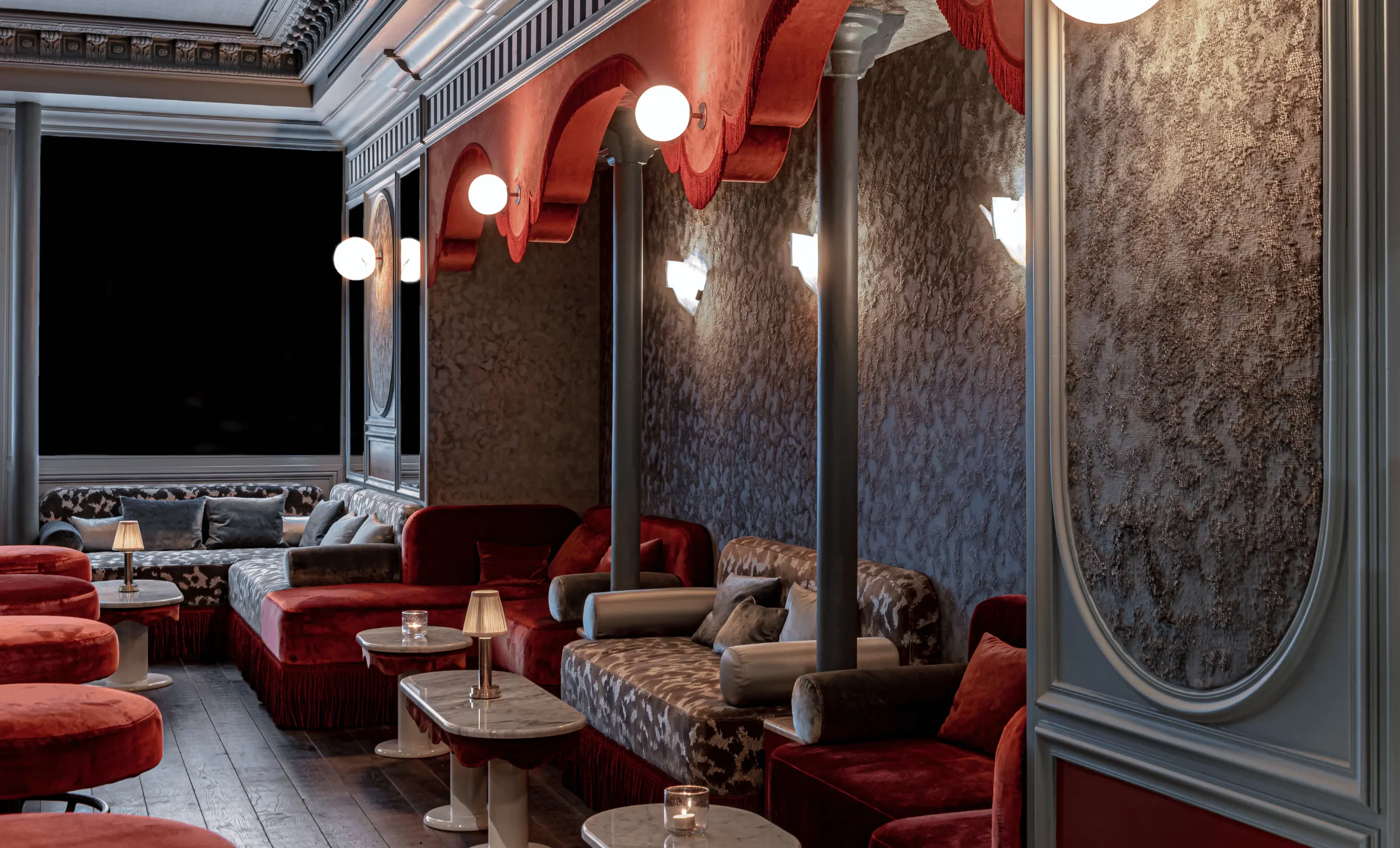 Elegant bar seating area featuring red velvet sofas, arched wall alcoves, and moody lighting at Experimental Group.