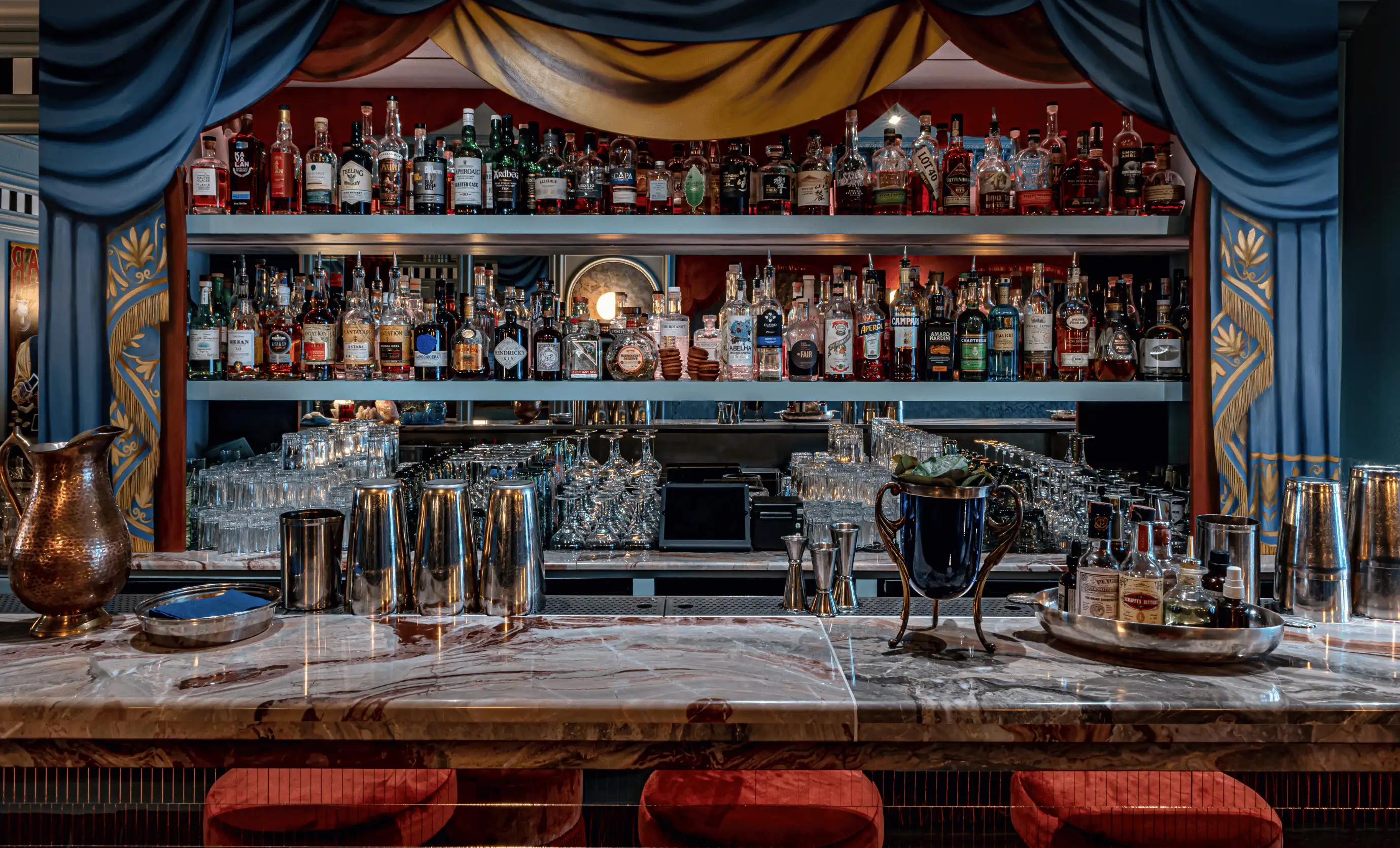 Well-stocked professional cocktail bar with blue velvet curtains and marble countertop at Experimental Group.