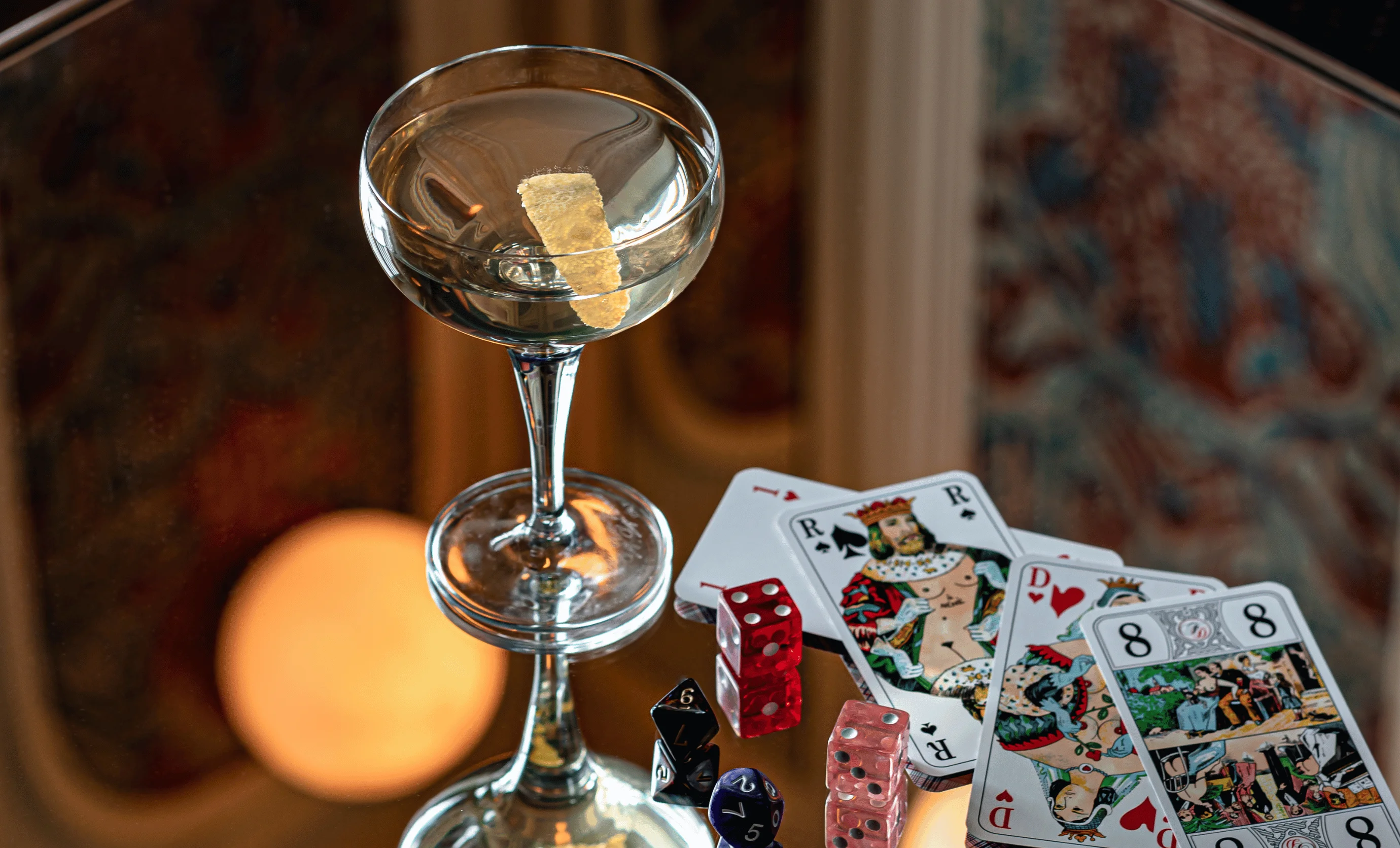 Sophisticated cocktail served in a coupe glass with playing cards and dice on a mirrored table at Experimental Group bar.