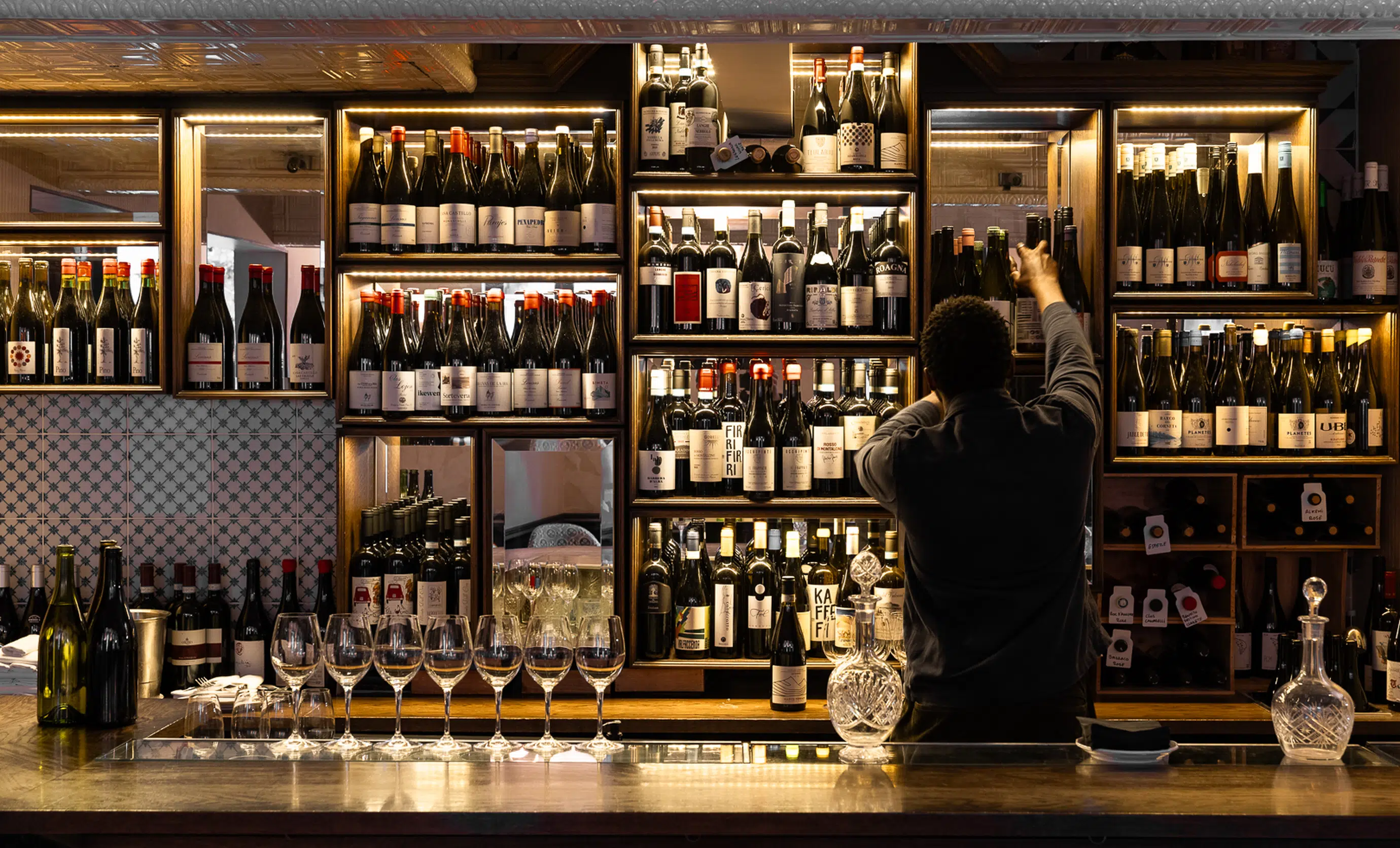 Bartender organizing wine bottles behind the bar counter at an Experimental Group establishment.