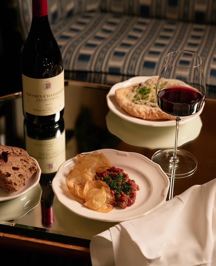 Close-up of Gevrey-Chambertin wine, tartare, and flatbread served on a mirrored table at an Experimental Group venue.