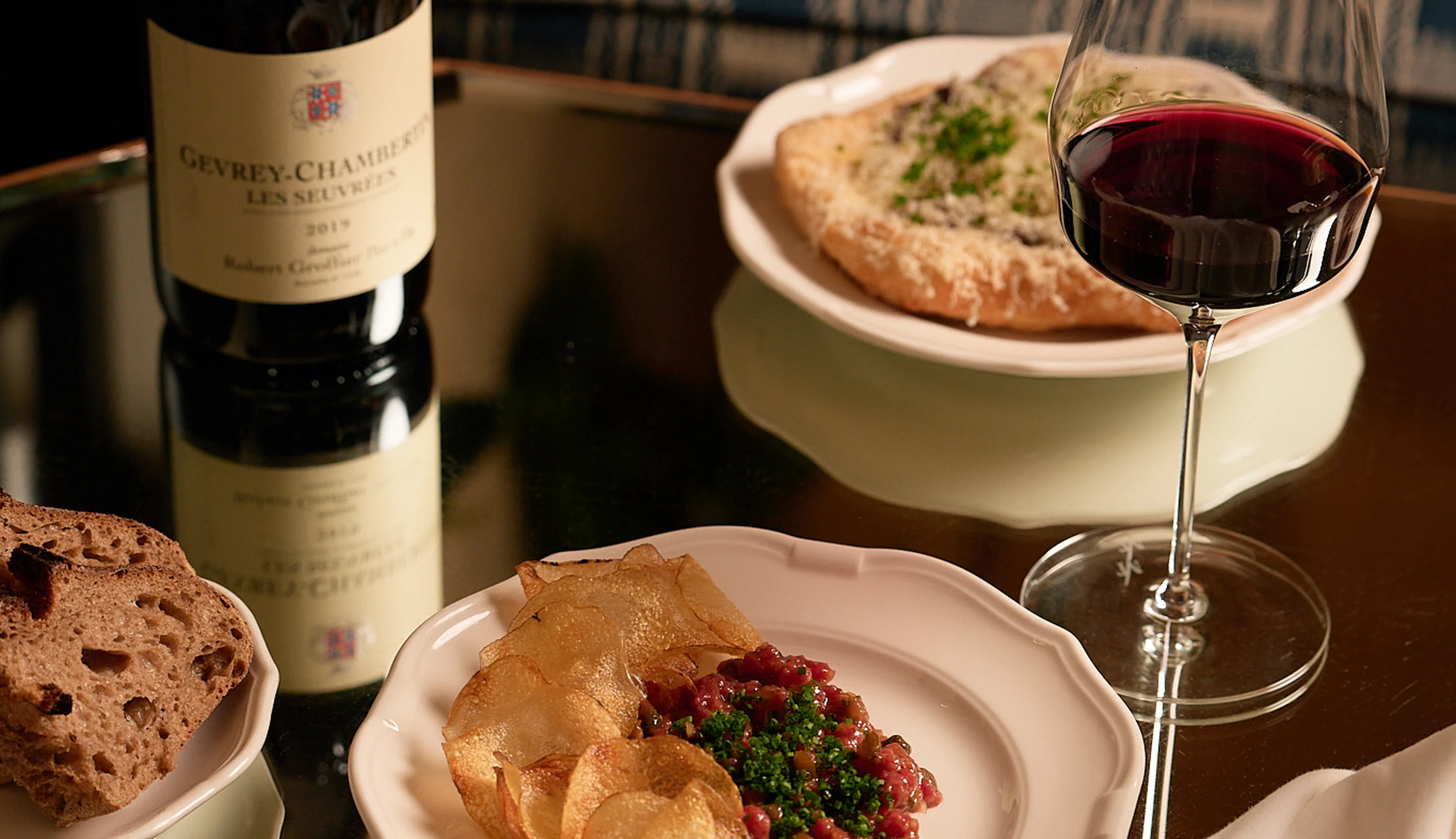 Gourmet tartare and a glass of Gevrey-Chambertin wine on a reflective table at an Experimental Group restaurant.