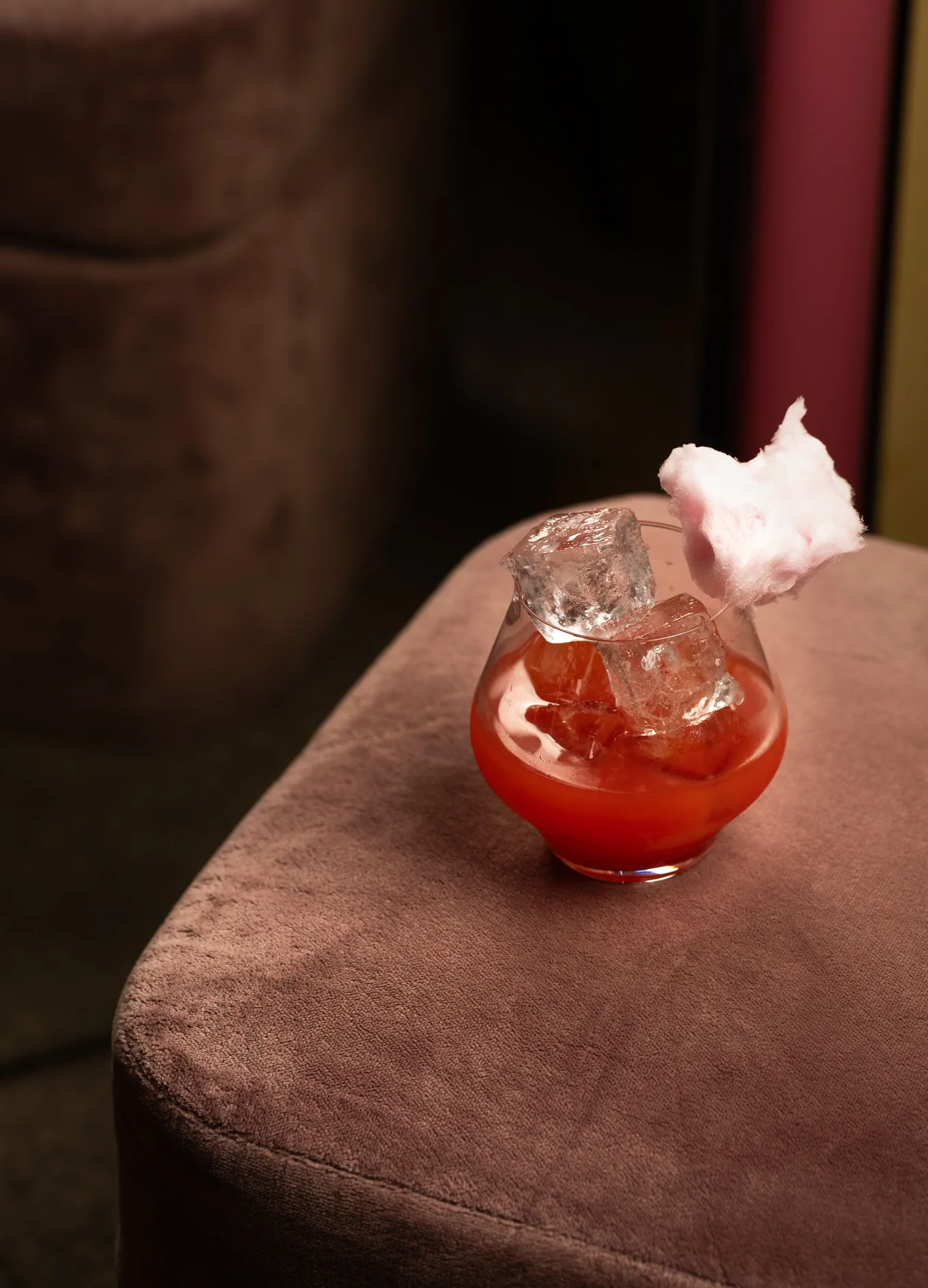 Creative red cocktail in a glass topped with pink cotton candy, served in an elegant Experimental Group lounge.