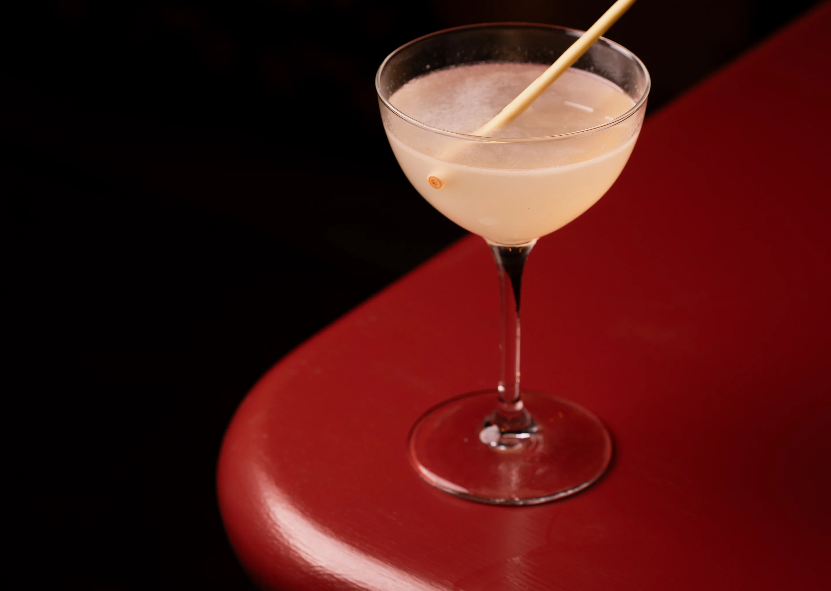 Close-up of a signature cocktail with a thin garnish resting on a vibrant red bar counter, highlighting the Experimental Group's mixology focus.