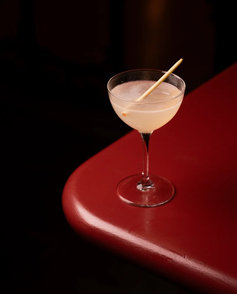 Minimalist craft cocktail served in a stemmed coupe glass on a sleek red bar top at an Experimental Group venue.