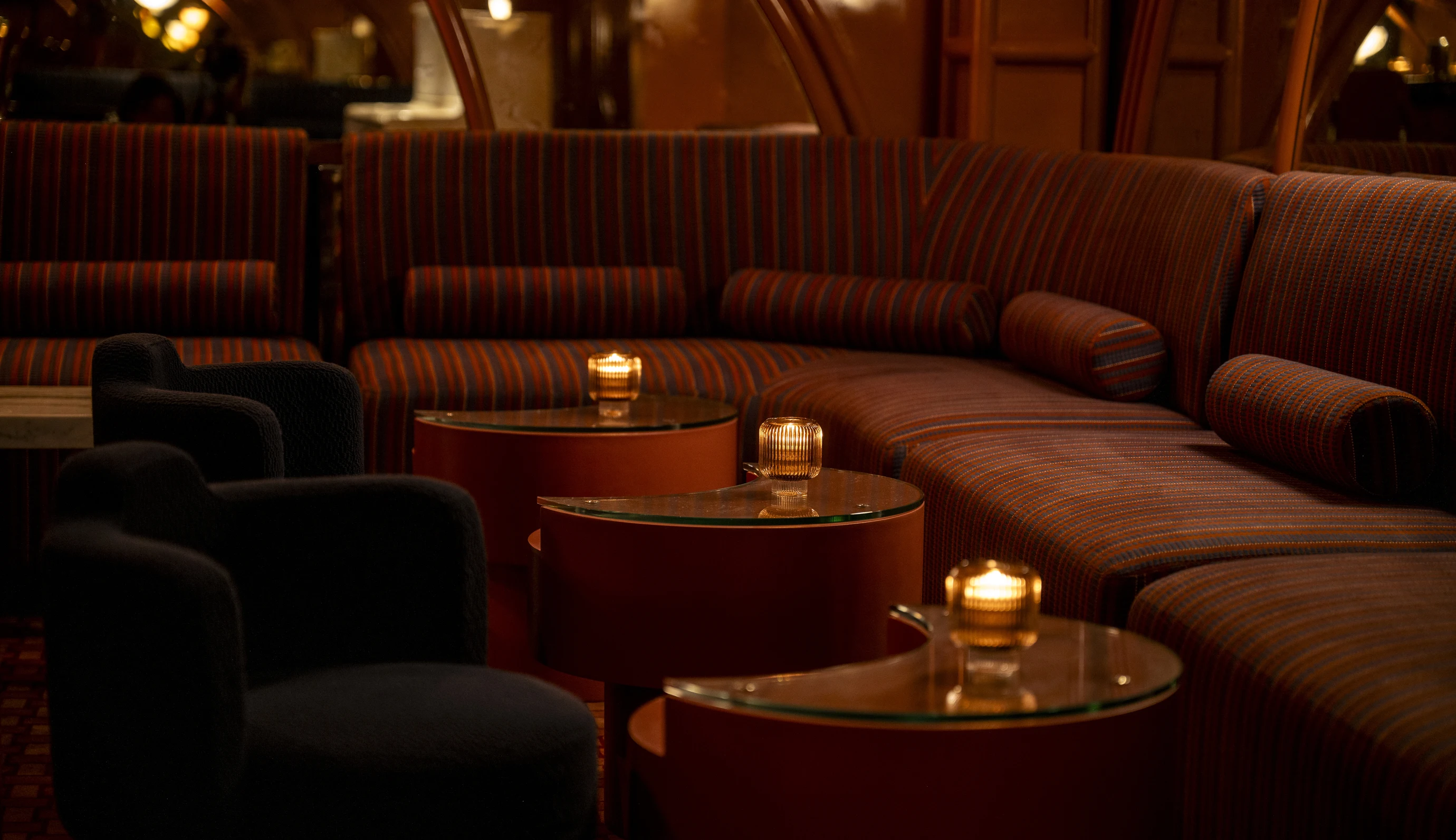 Elegant lounge area at an Experimental Group property with semi-circular tables, plush striped seating, and intimate candle lighting.