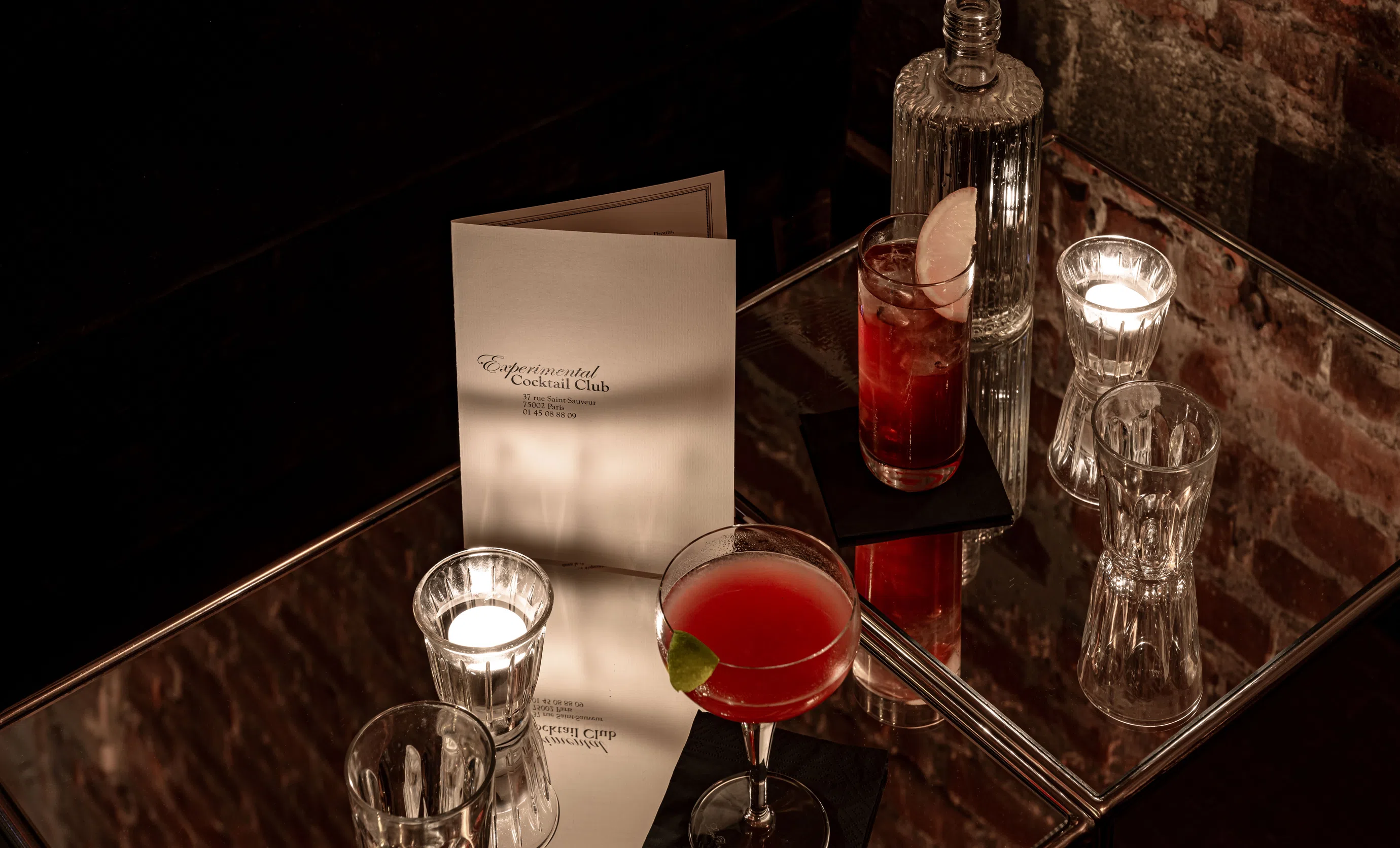 A cocktail menu and crafted drinks on a mirrored table at Experimental Cocktail Club in Paris.