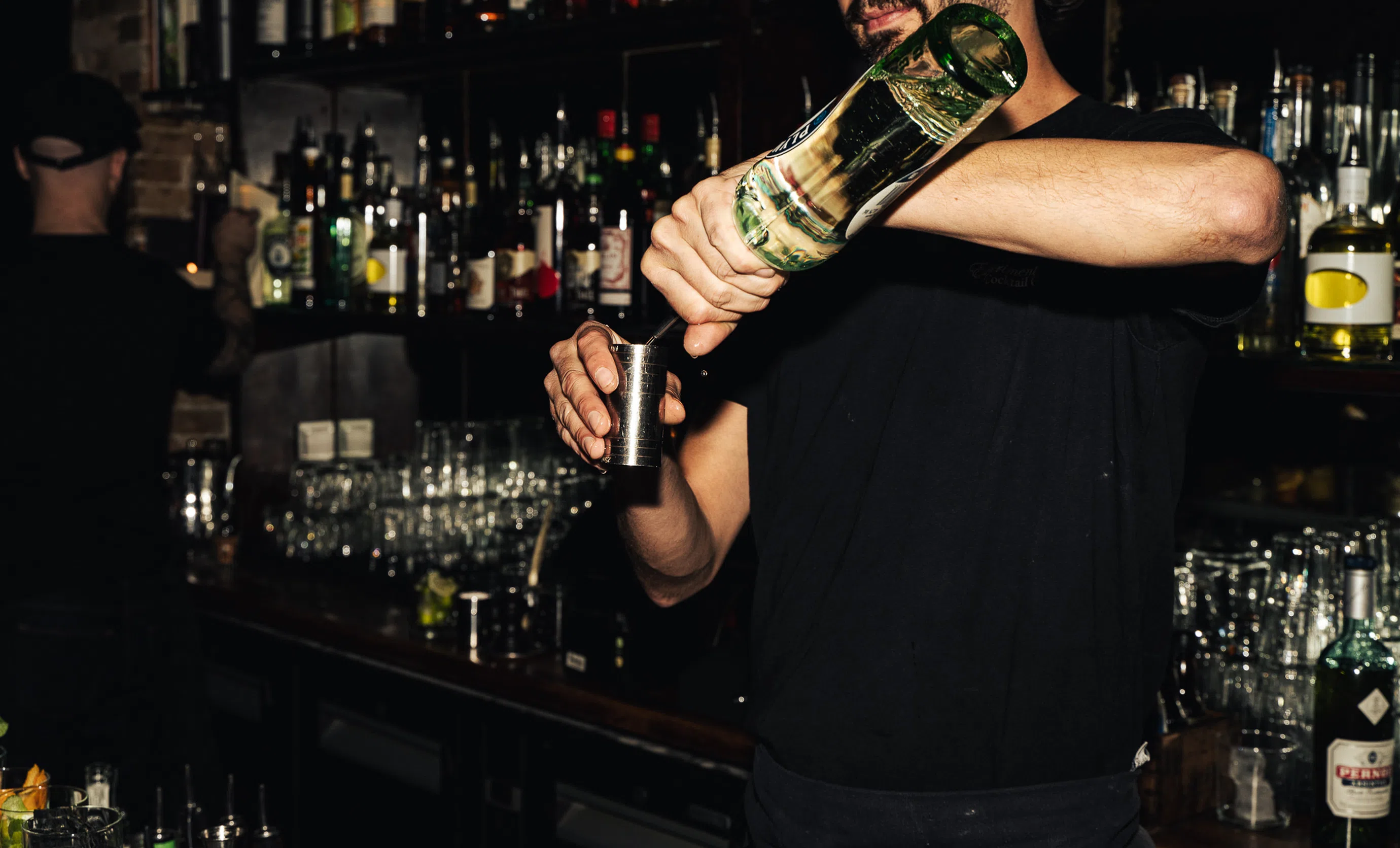 Bartender pouring a cocktail from a spirit bottle into a jigger at Experimental Cocktail Club.