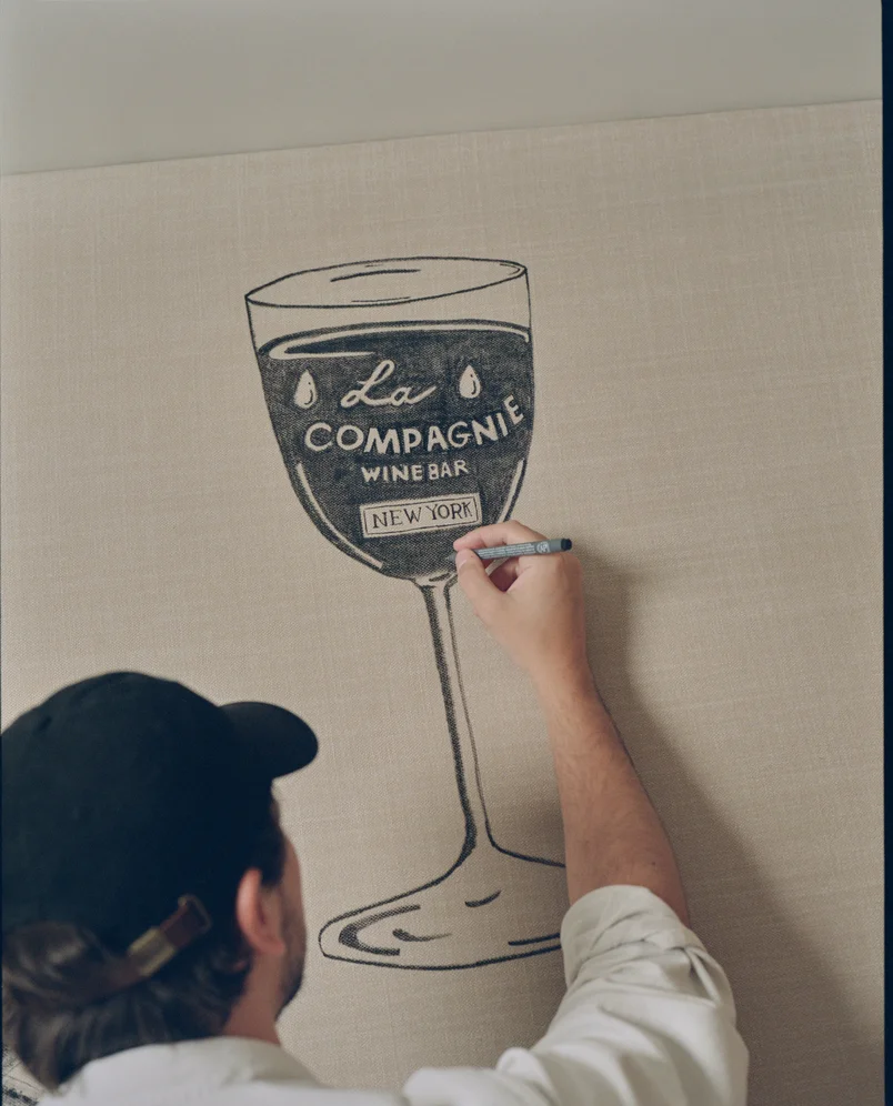 Artist drawing the La Compagnie Wine Bar New York logo on a wall, showcasing the craftsmanship of the Experimental Group.