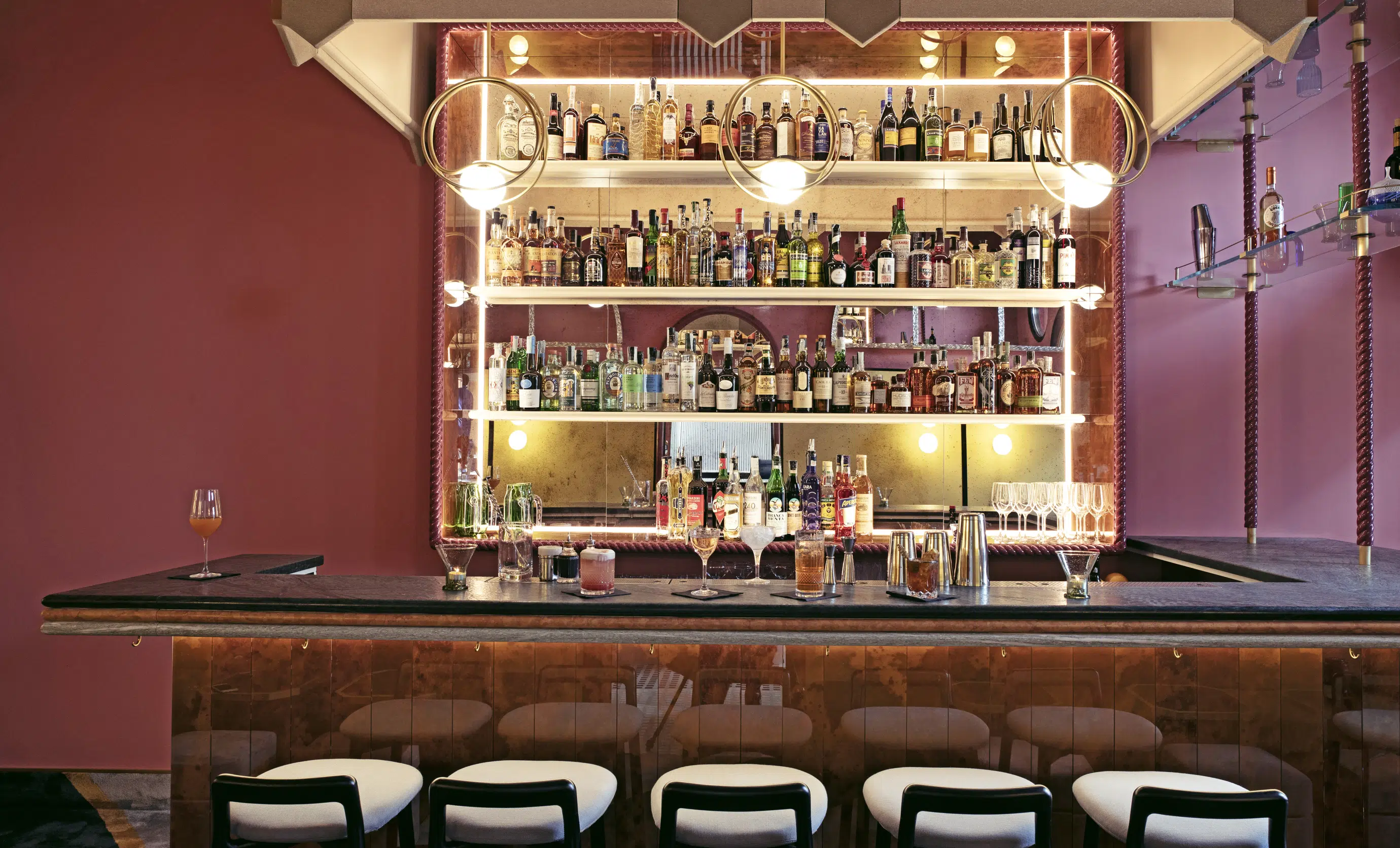 Interior of an Experimental Group bar featuring a counter, designer bar stools, and backlit wall shelves.