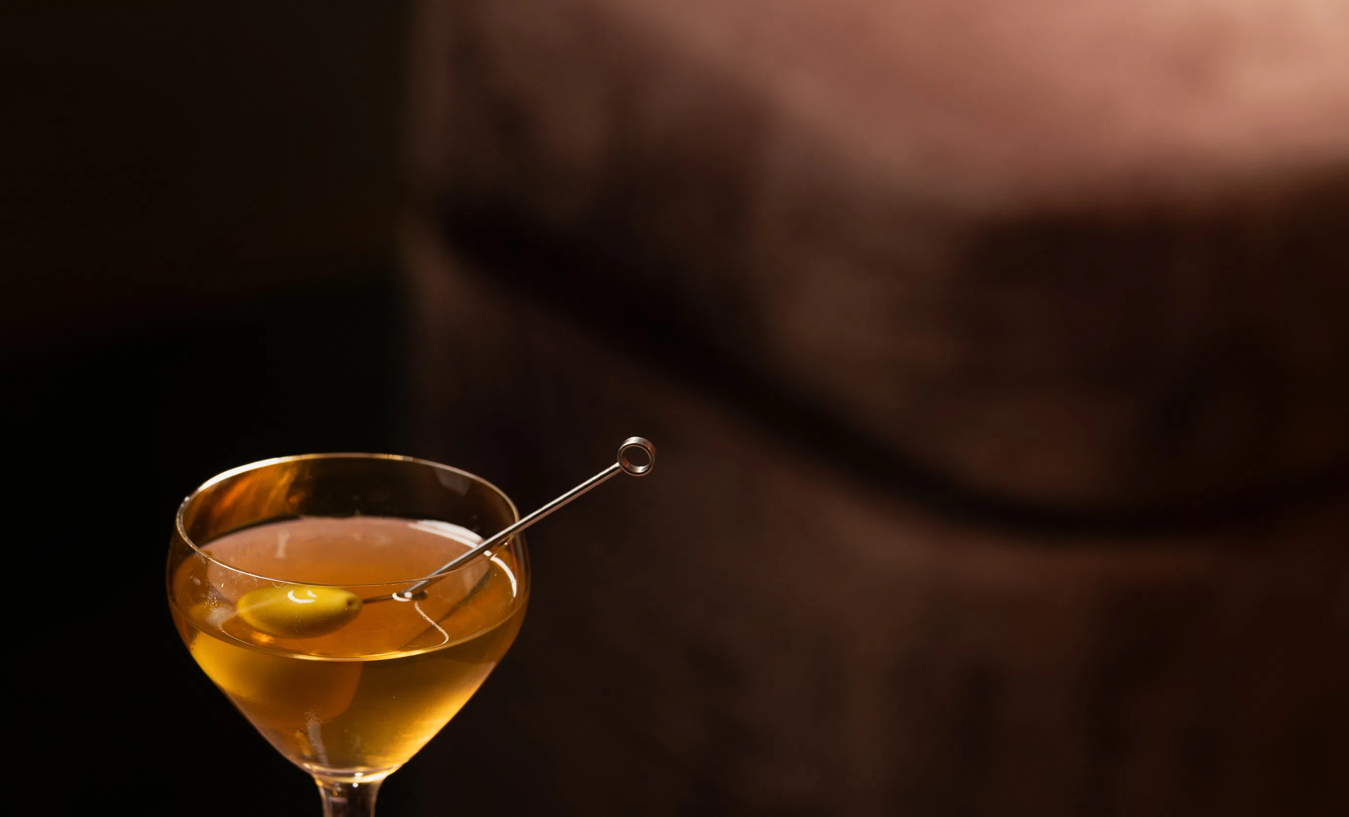 Cocktail served in an elegant coupe glass with an olive, dim lighting at an Experimental Group bar.