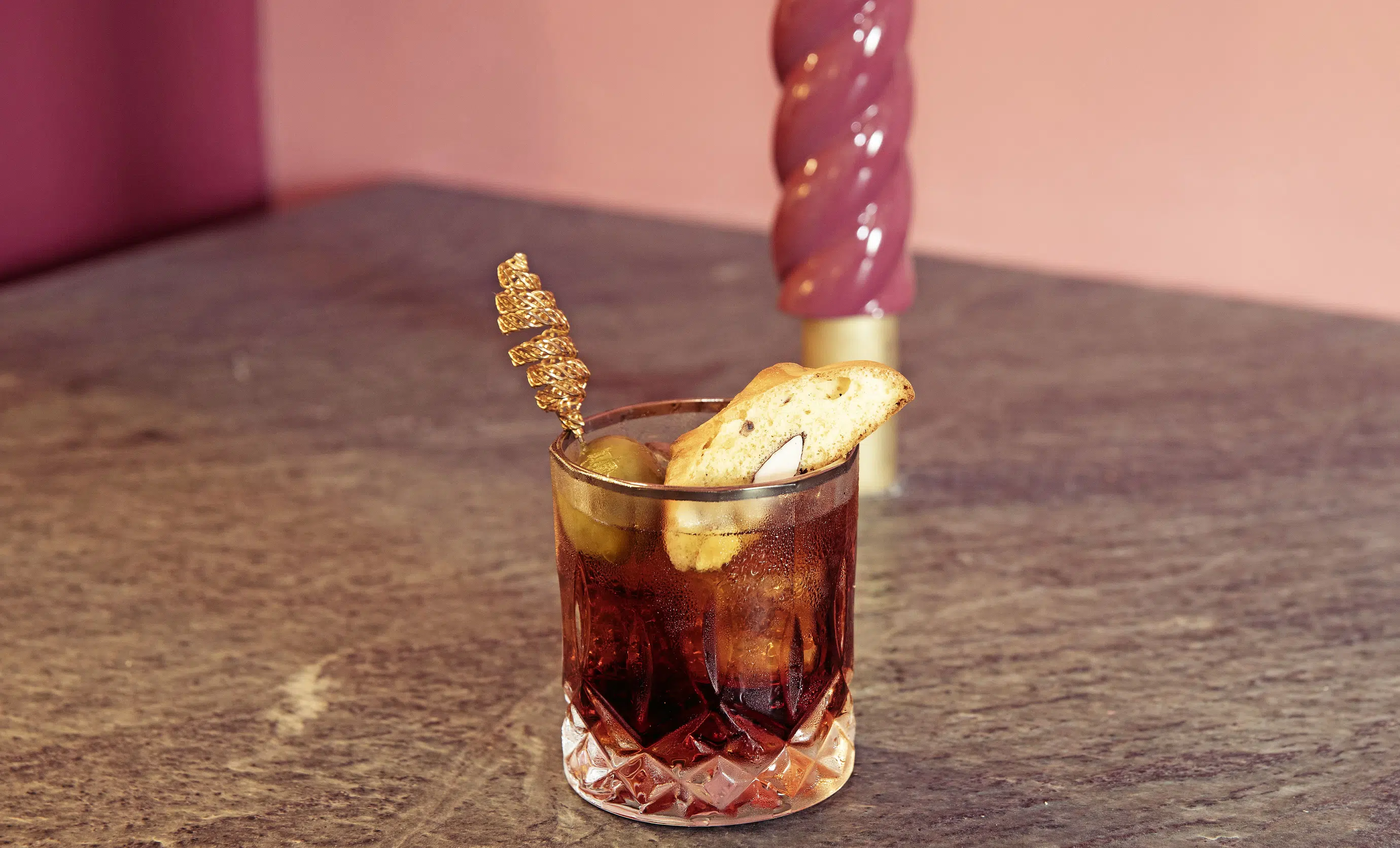 Sophisticated cocktail garnished with an olive and a biscotti, presented on a counter at an Experimental Group establishment.