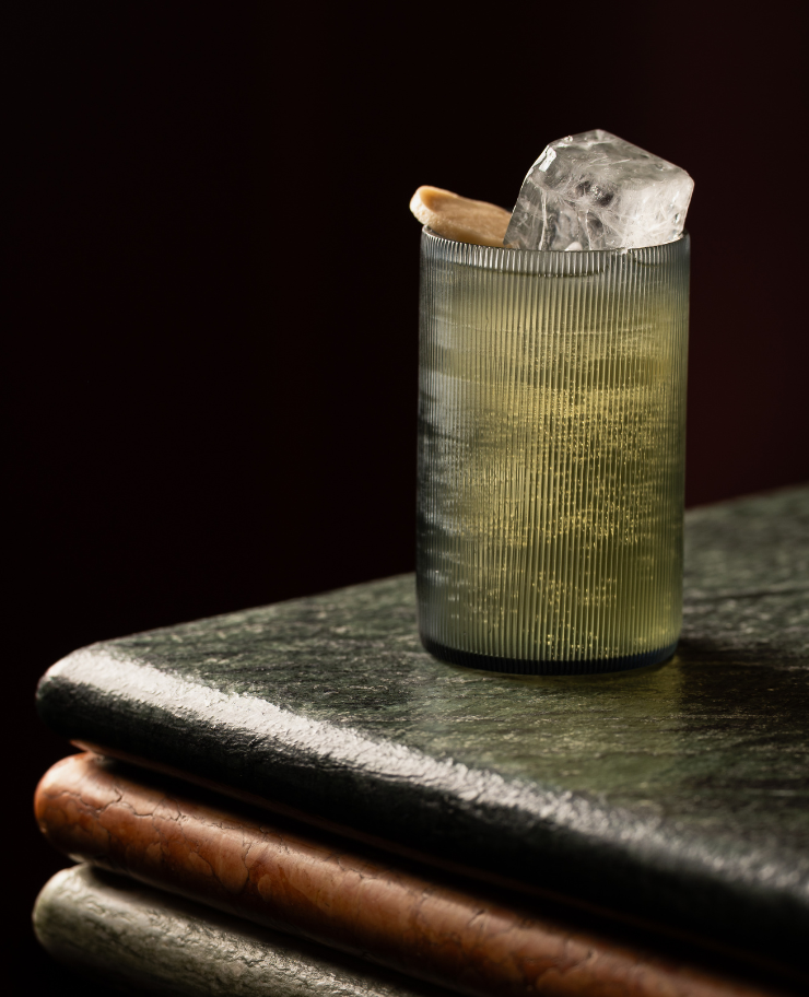 Refreshing cocktail in a ribbed glass with a large ice cube, served on a marble counter at an Experimental Group bar.