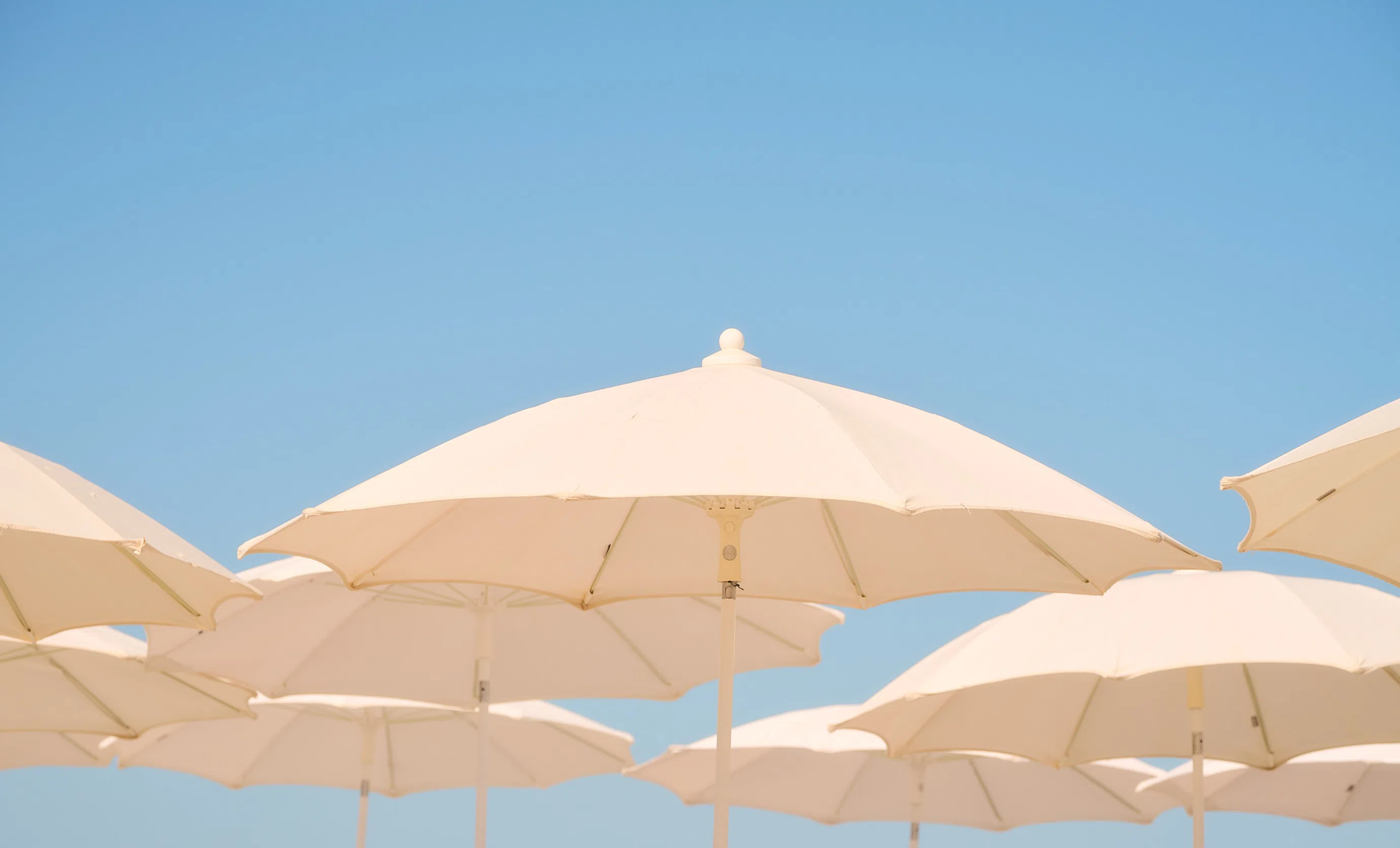 Detail of elegant white umbrellas under an azure blue sky at an Experimental Group seaside resort.