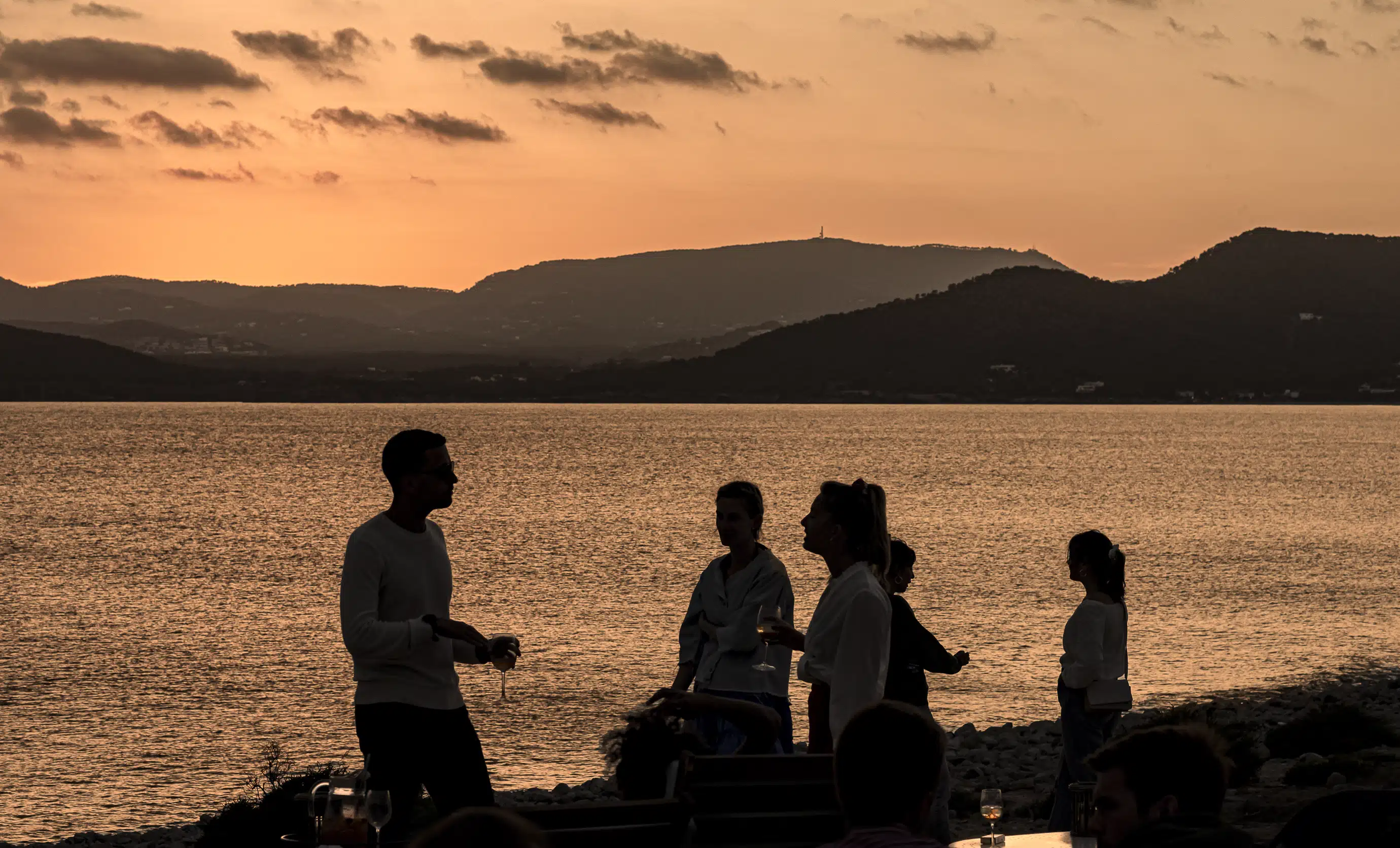 Relaxed atmosphere at sunset with guests enjoying a cocktail by the water, Experimental Group Ibiza.