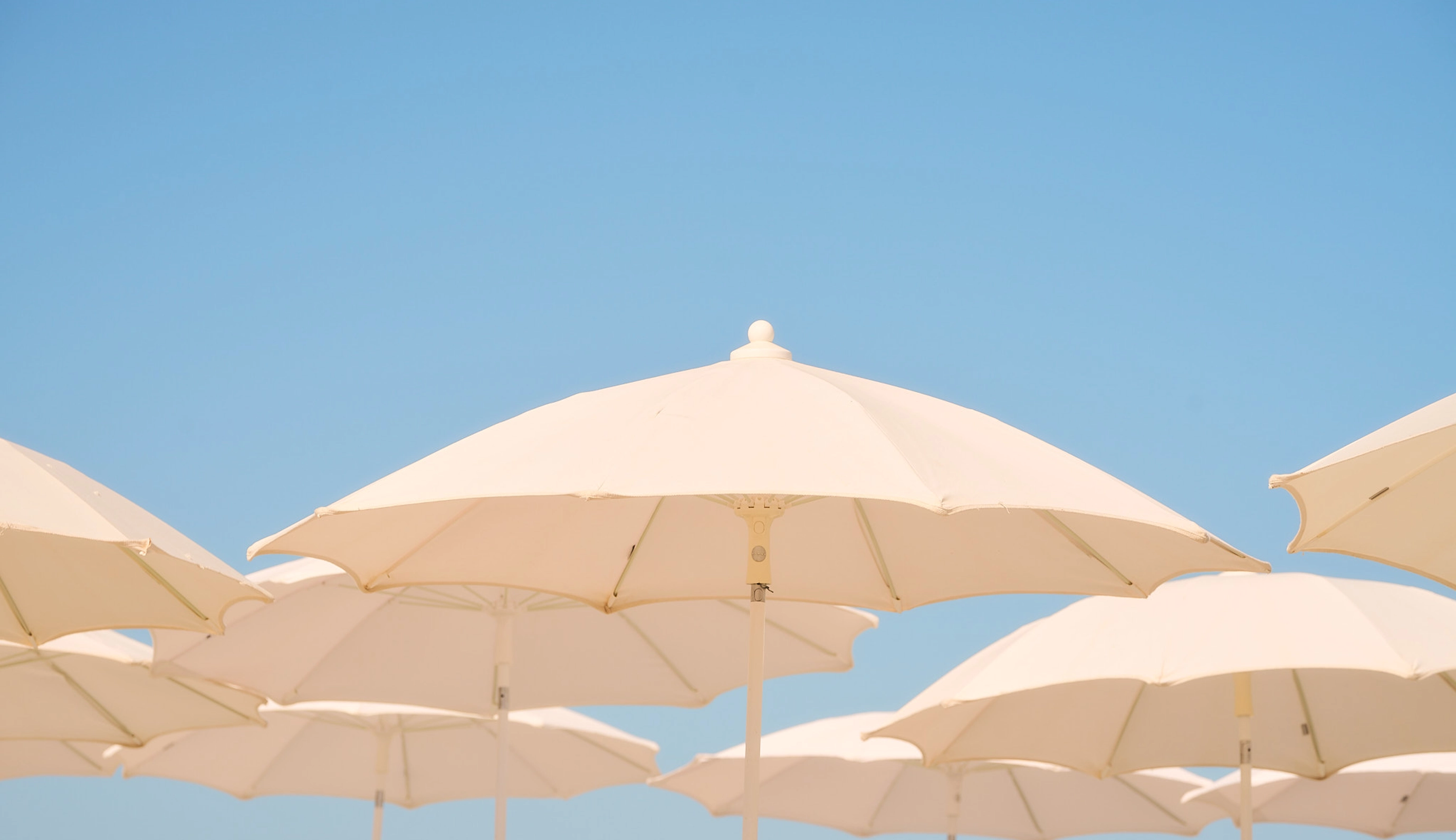 View of elegant white parasols against a vibrant blue sky, capturing the relaxing atmosphere of an Experimental Group property.