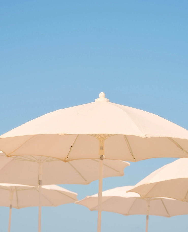 Minimalist white beach umbrellas under a clear blue sky at an Experimental Group destination.