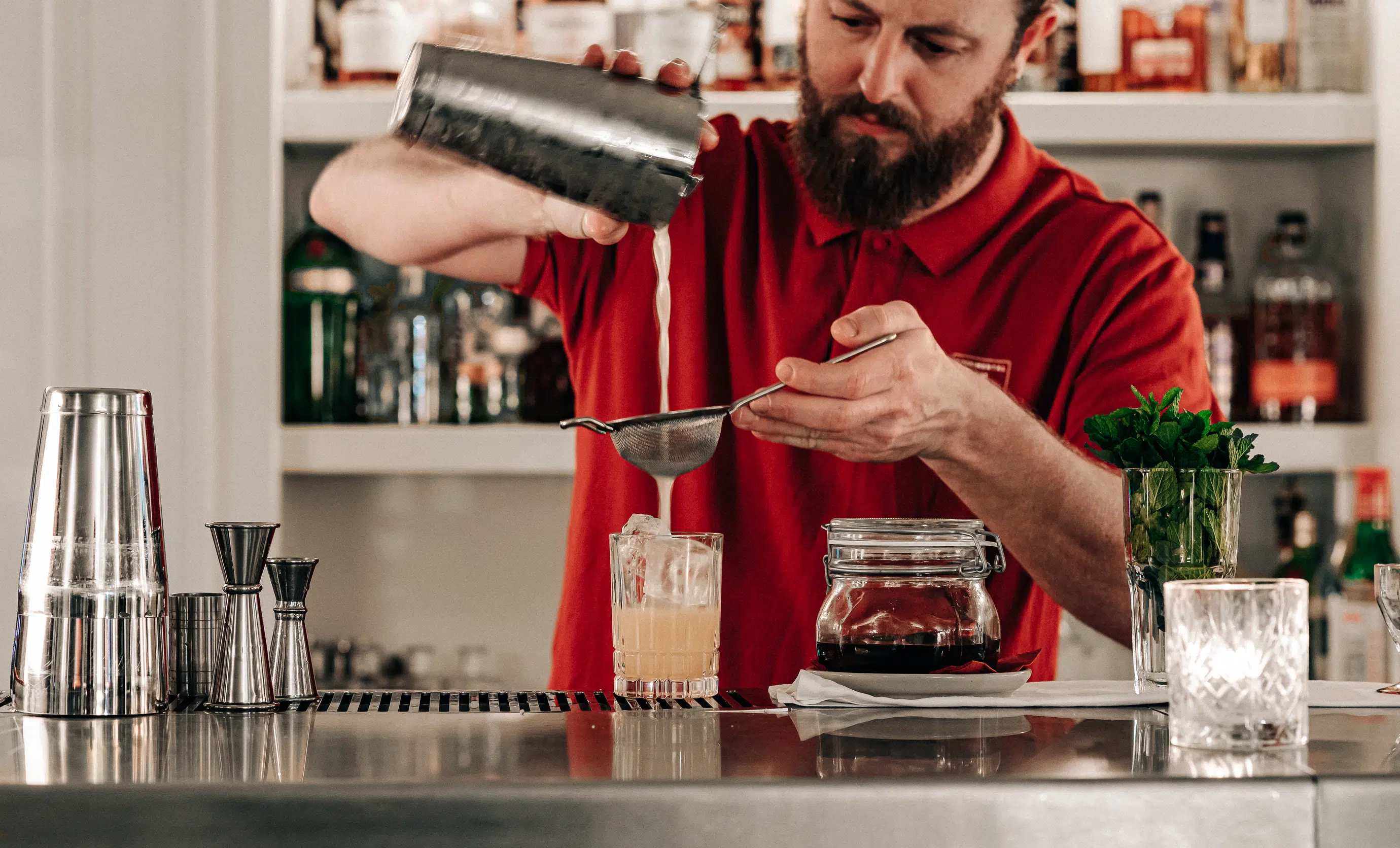Bartender straining a signature craft cocktail behind the bar at the Experimental Chalet in Verbier.