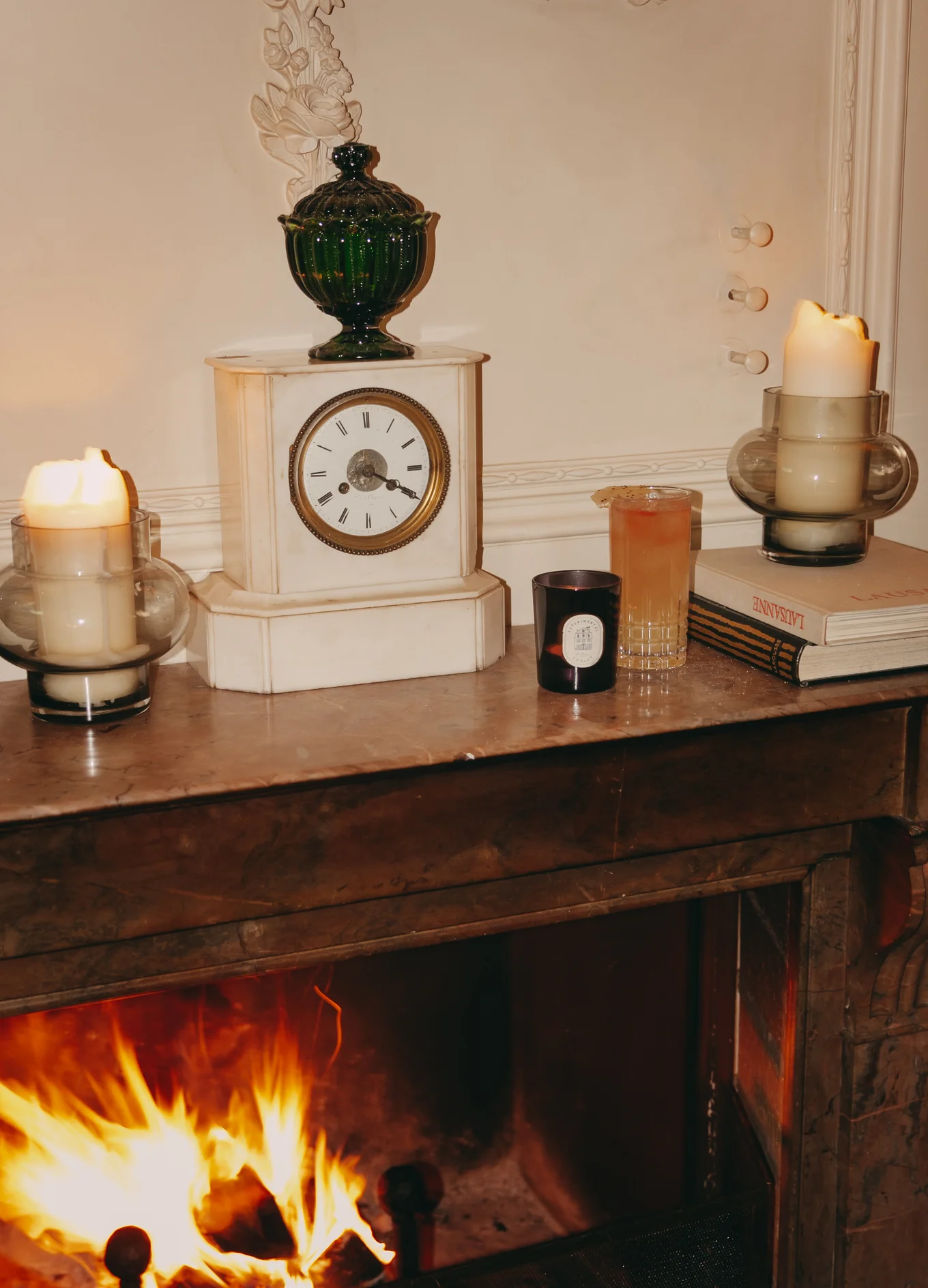 Warm fireplace ambiance with a mantel clock, scented candle, and cocktails at the Experimental Cocktail Club, Verbier.