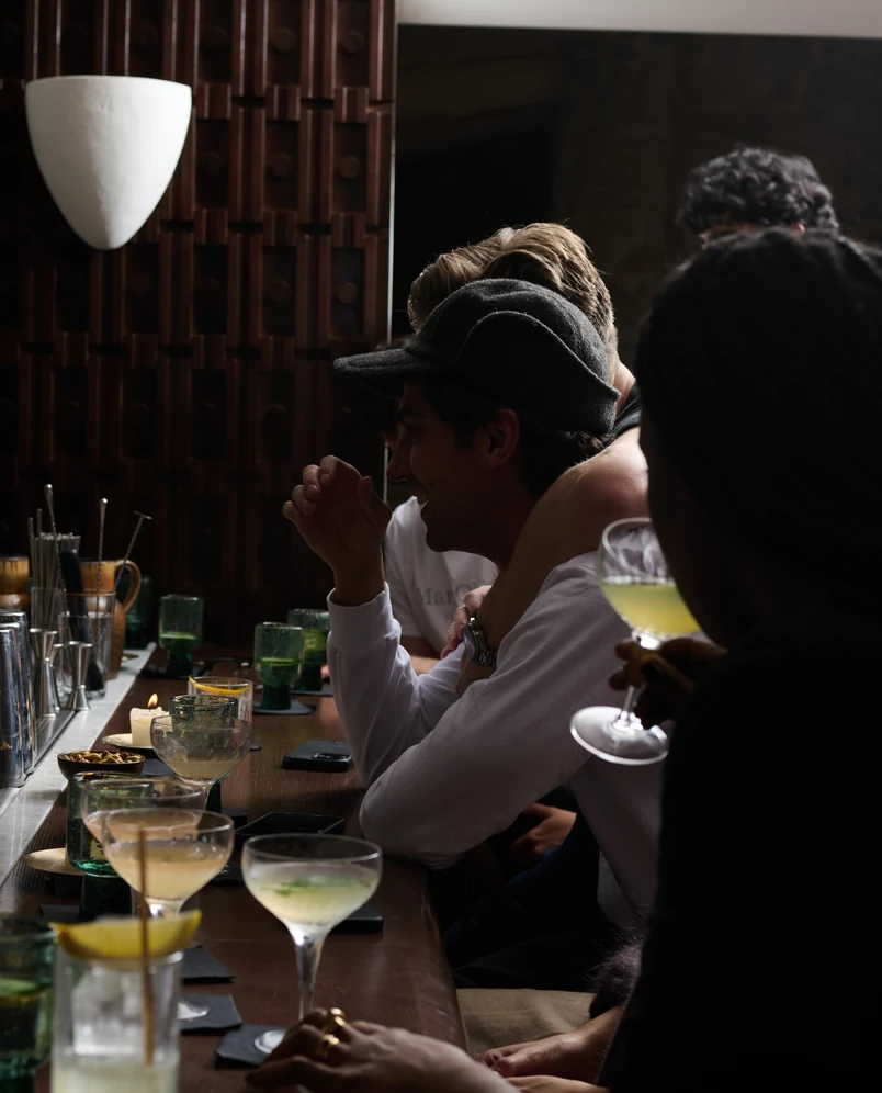 Close-up of cocktails on the bar counter with guests laughing in the background at the Experimental Chalet.